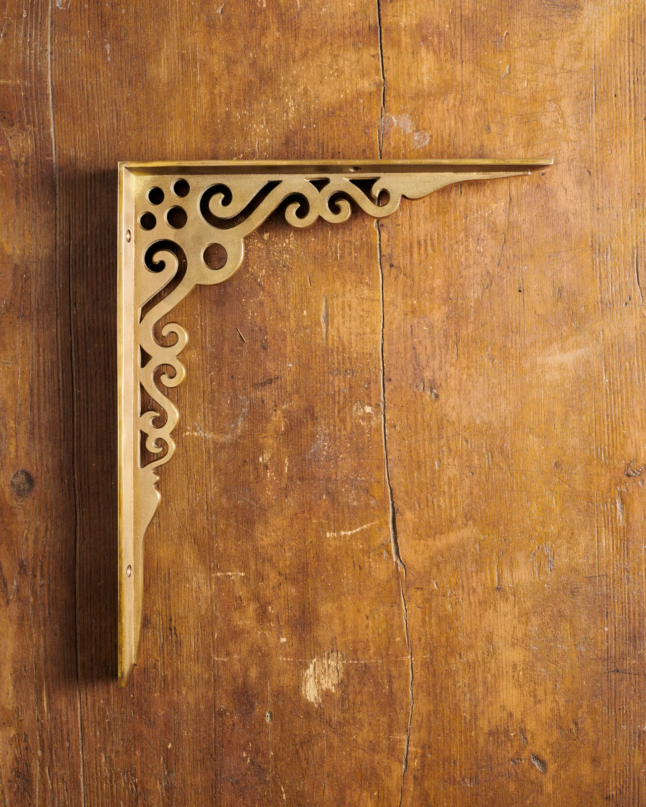 A side profile view of a large Victorian-inspired ornate shelf bracket in an aged brass finish.