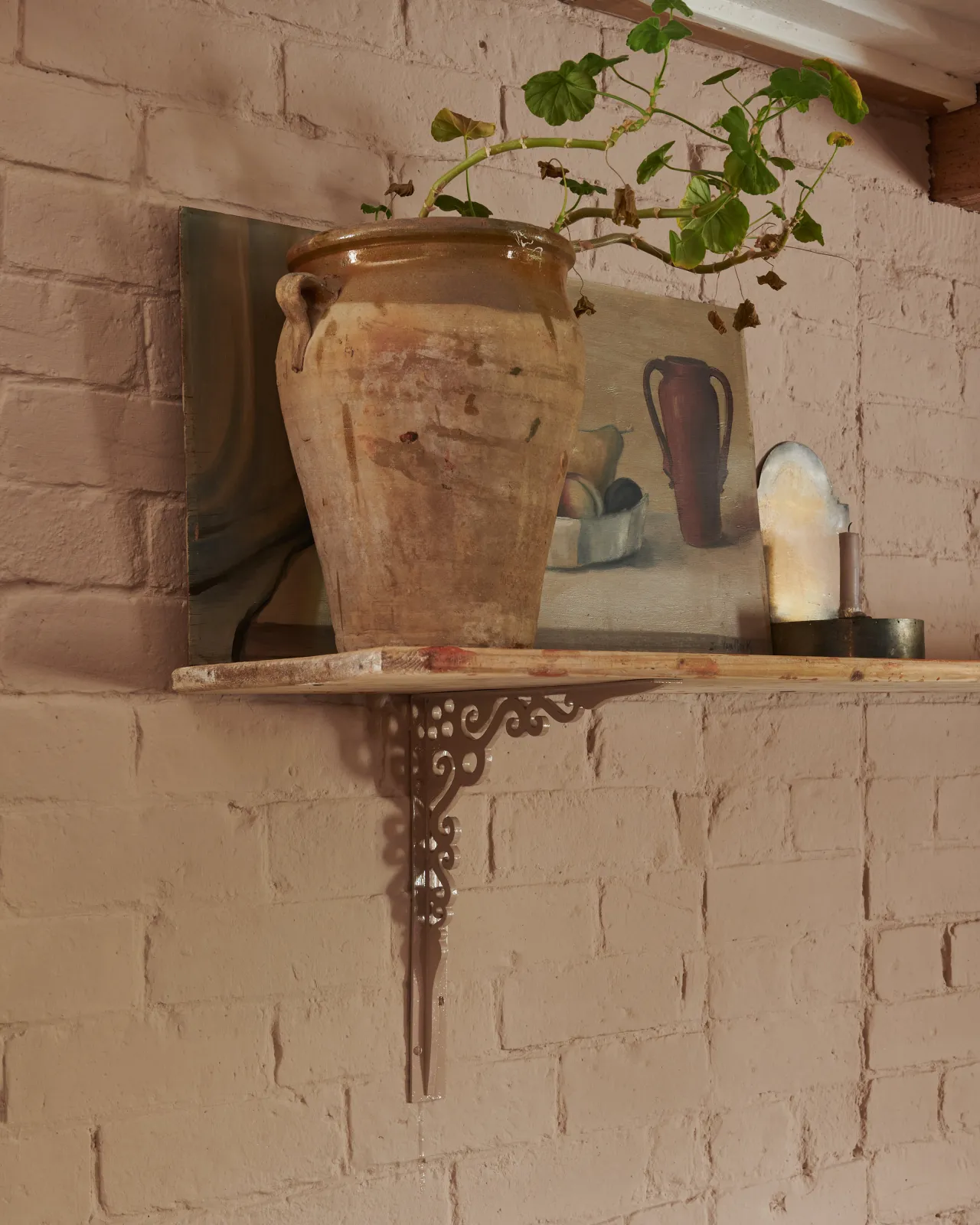 An oblique view of a large Victorian-inspired ornate pink painted shelf bracket holding a deep pine shelf to a pink colour brick wall.