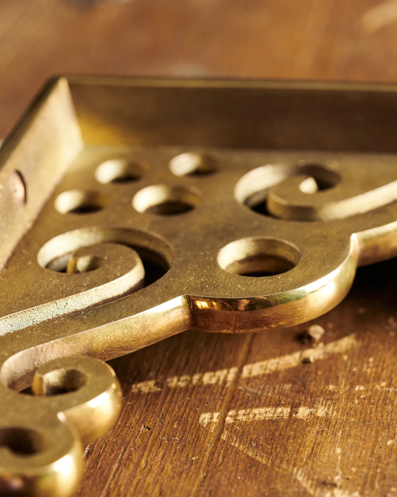 A close-up view of the decorative cutout patterns on a large Victorian-inspired ornate aged brass shelf bracket.
