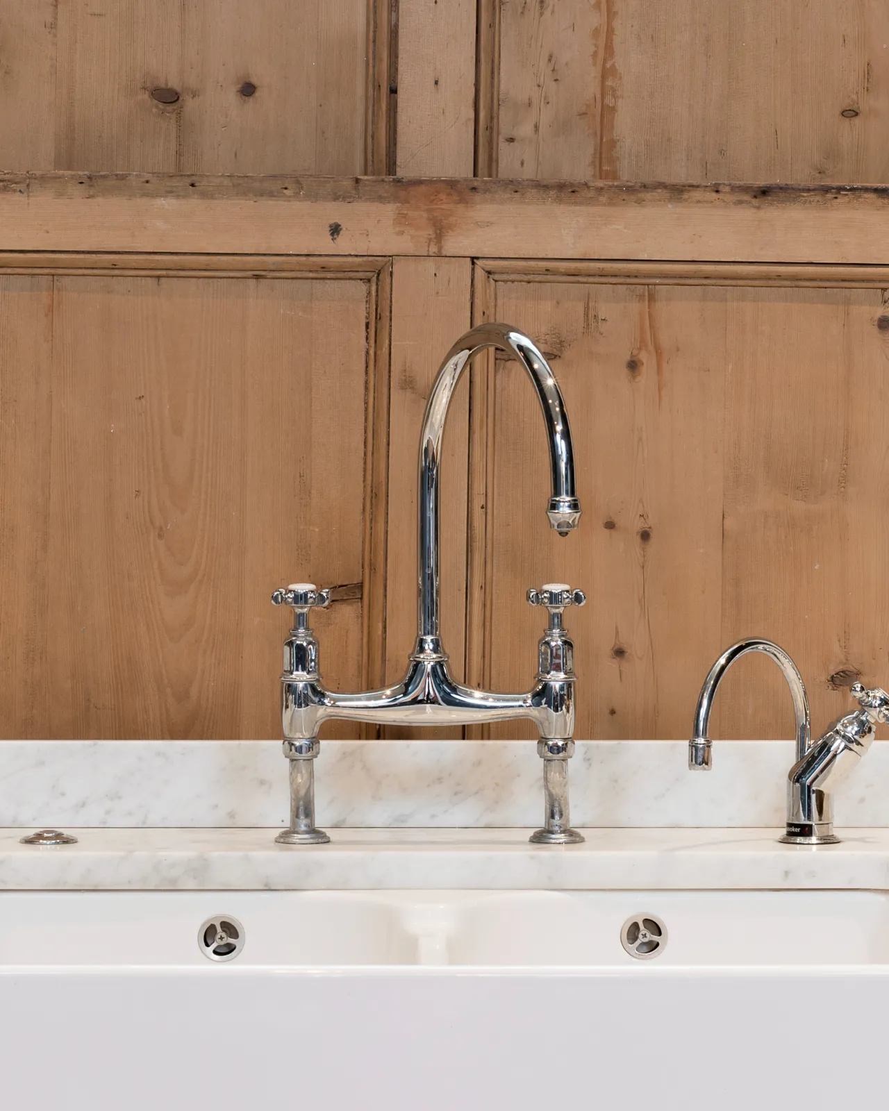 A straight-on view of a traditional-style chrome mixer tap with crosshead handles with traditional pine shutters behind.