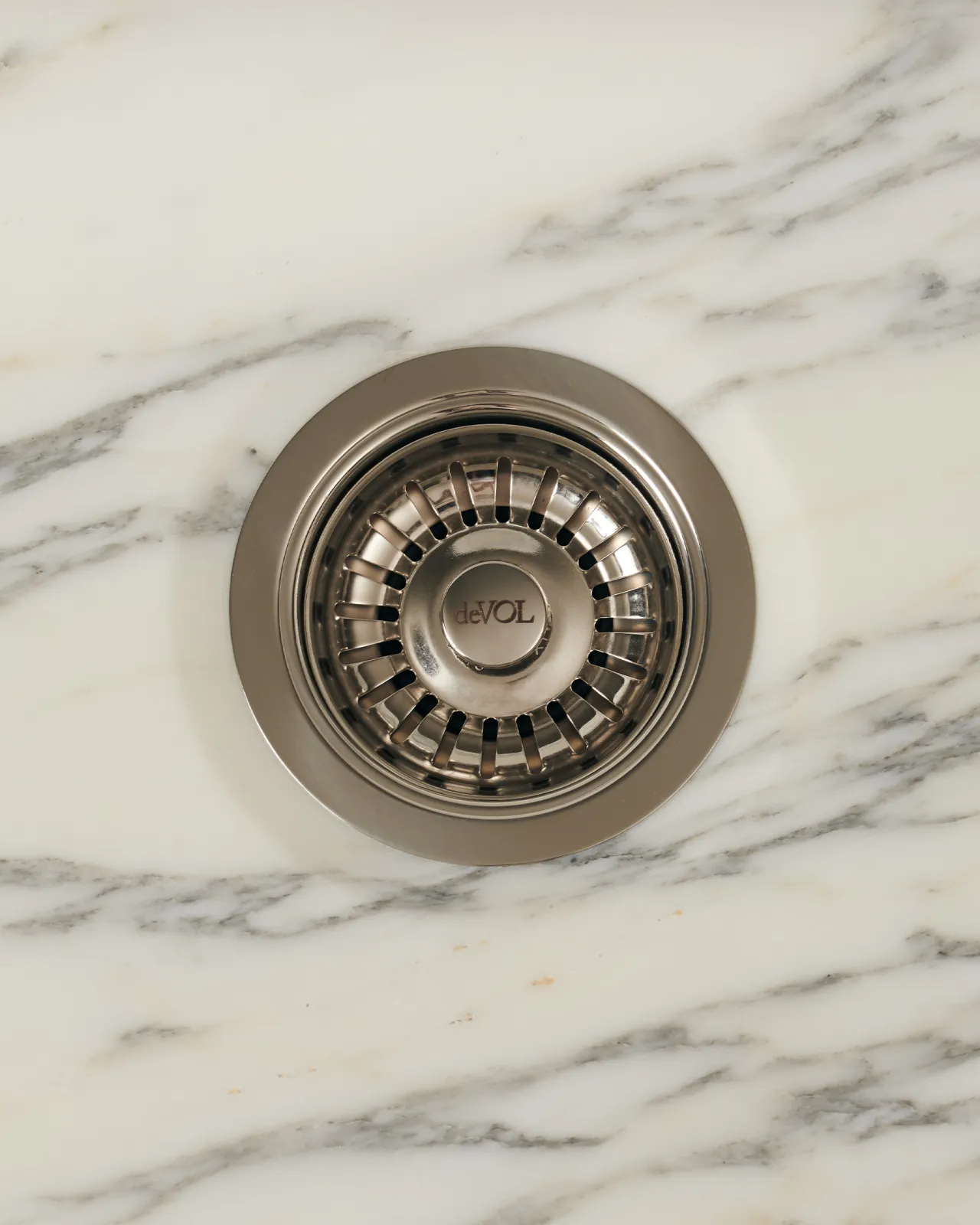 An overhead view of a basket waste strainer in a polished chrome finish, there is a small 'deVOL' logo in the middle of the central finial.