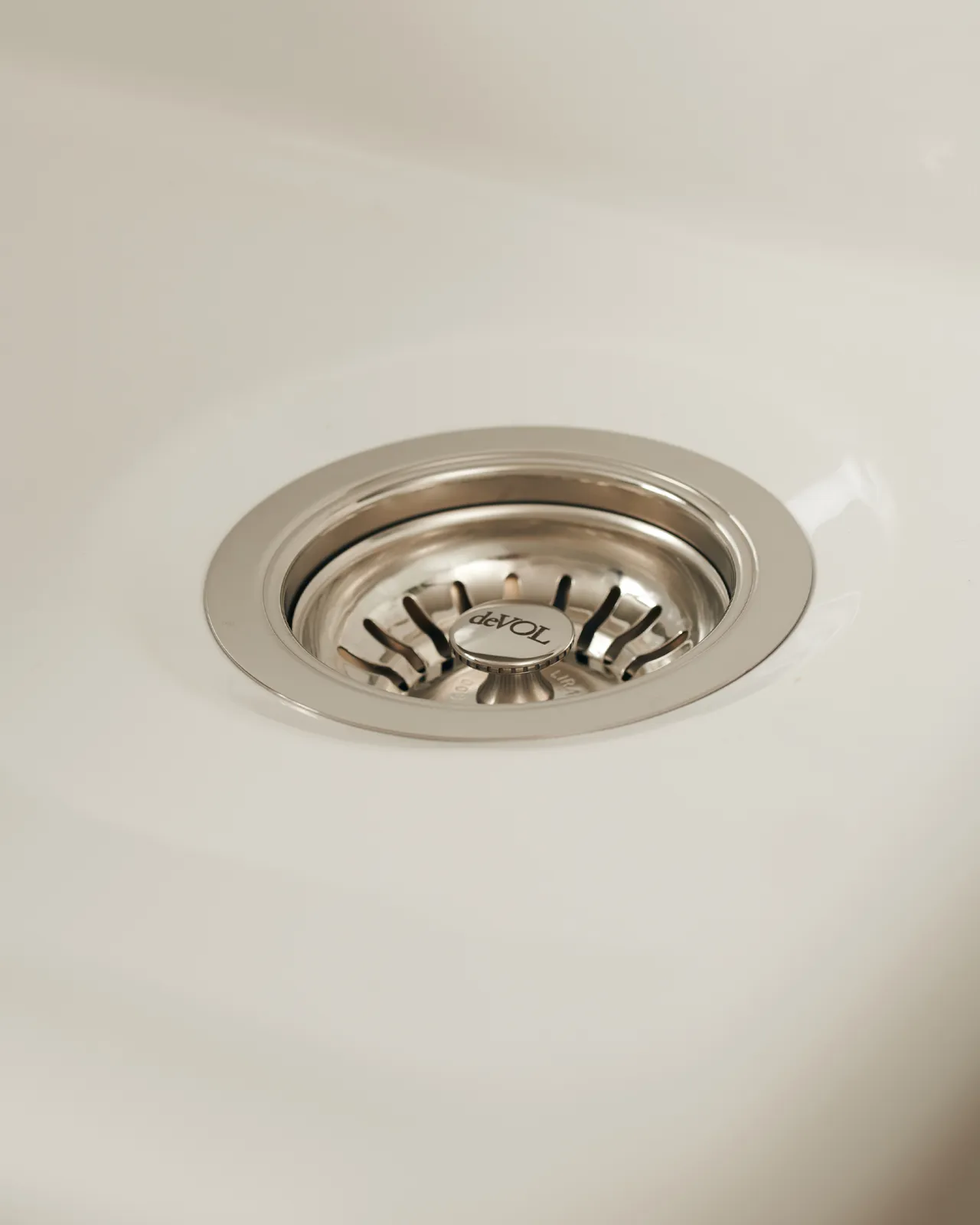 A basket waste strainer in a polished chrome finish fitted in a ceramic sink.
