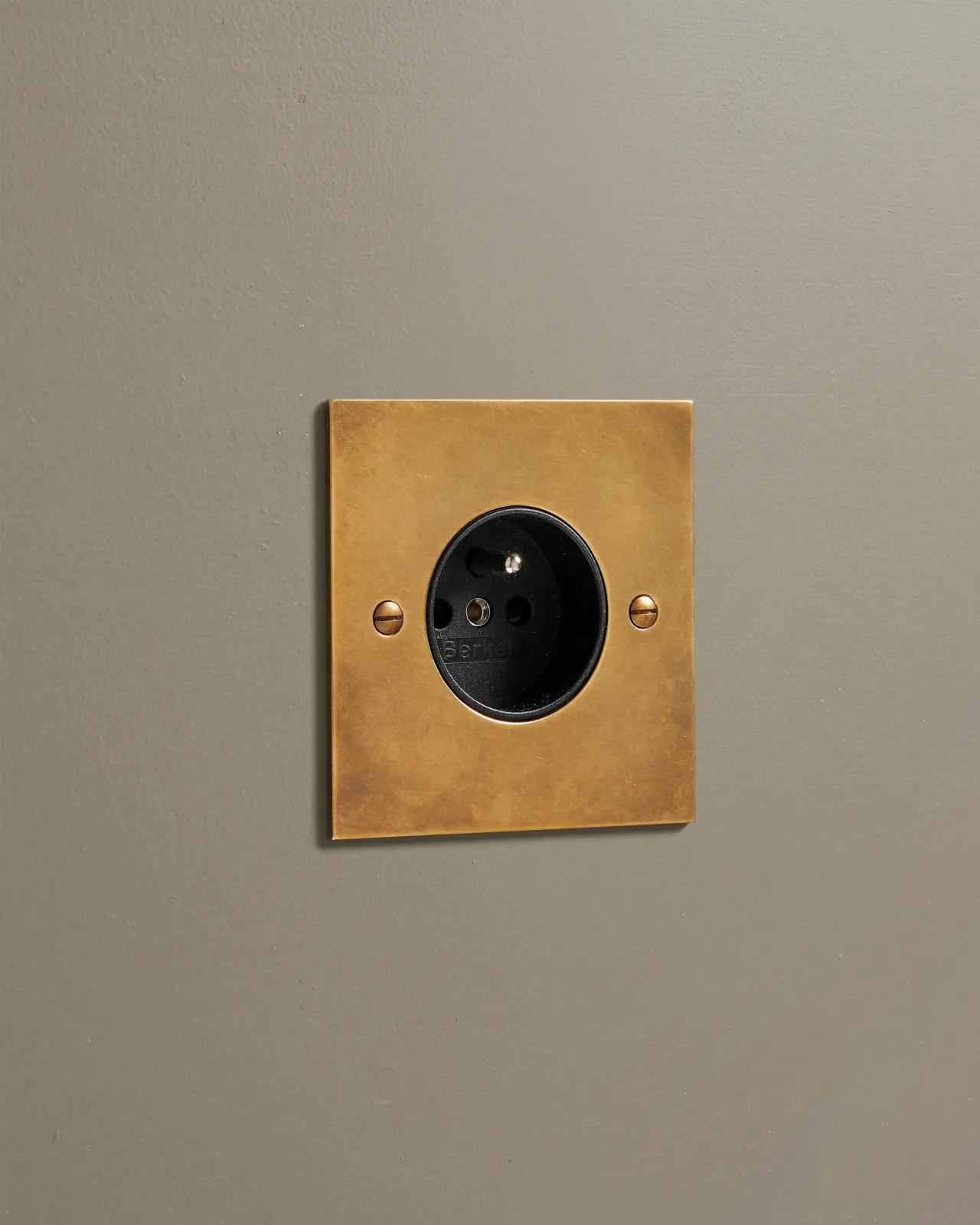 An oblique view of a classic French-style single plug socket in a warm burnished brass finish.