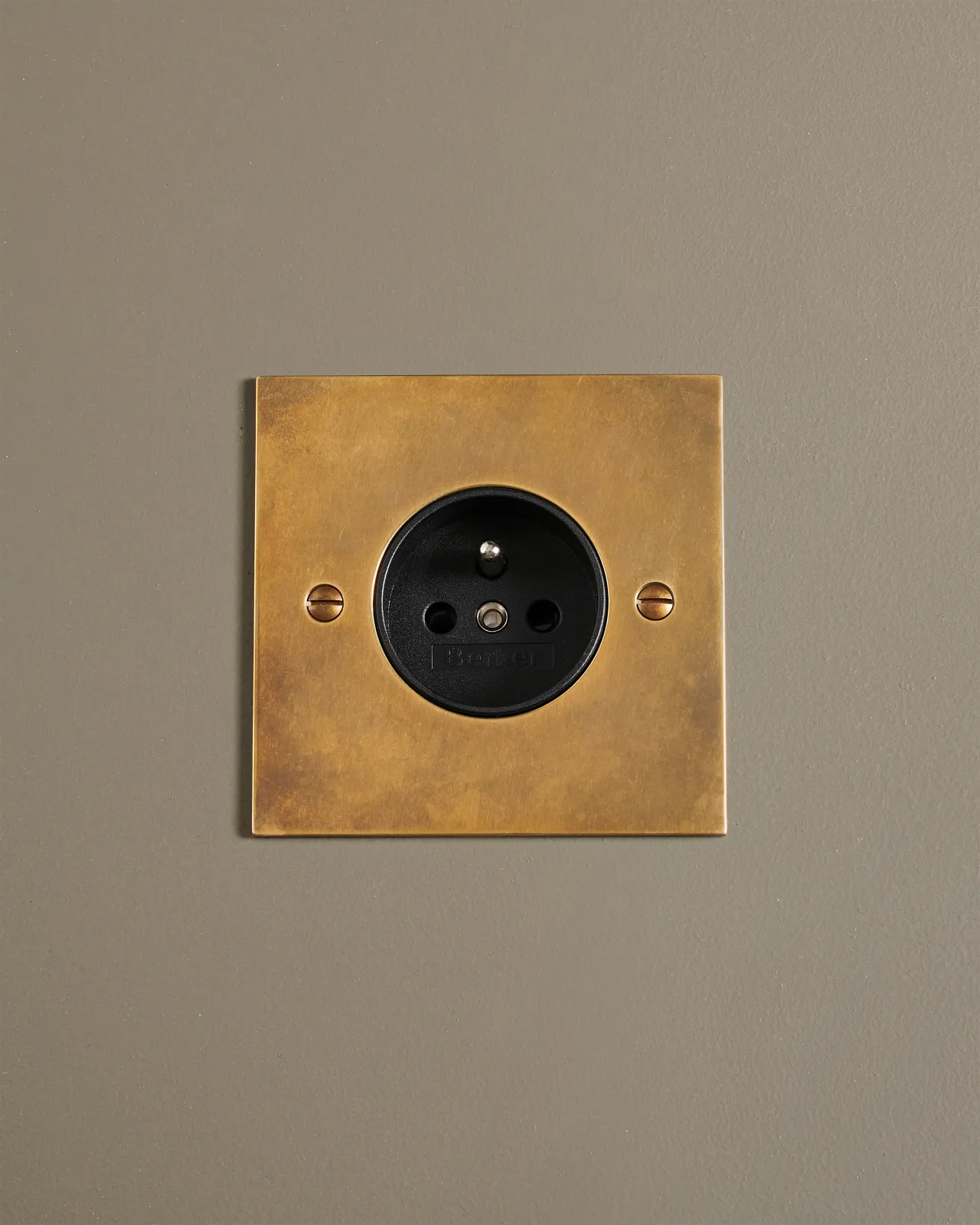 A straight-on view of a classic French-style single plug socket in a warm burnished brass finish.