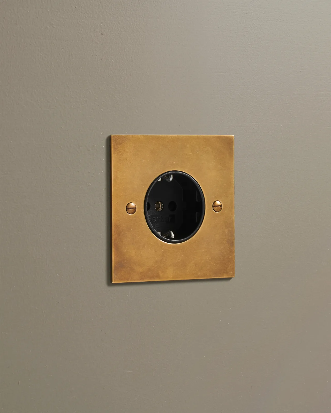 An oblique view of a classic Schuko-style single plug socket in a warm burnished brass finish.