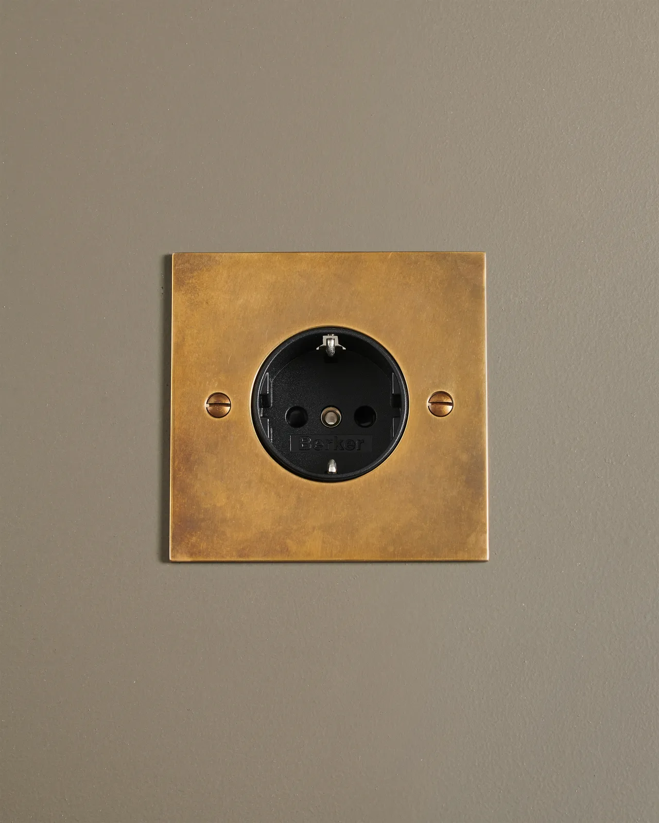 A straight-on view of a classic Schuko-style single plug socket in a warm burnished brass finish.