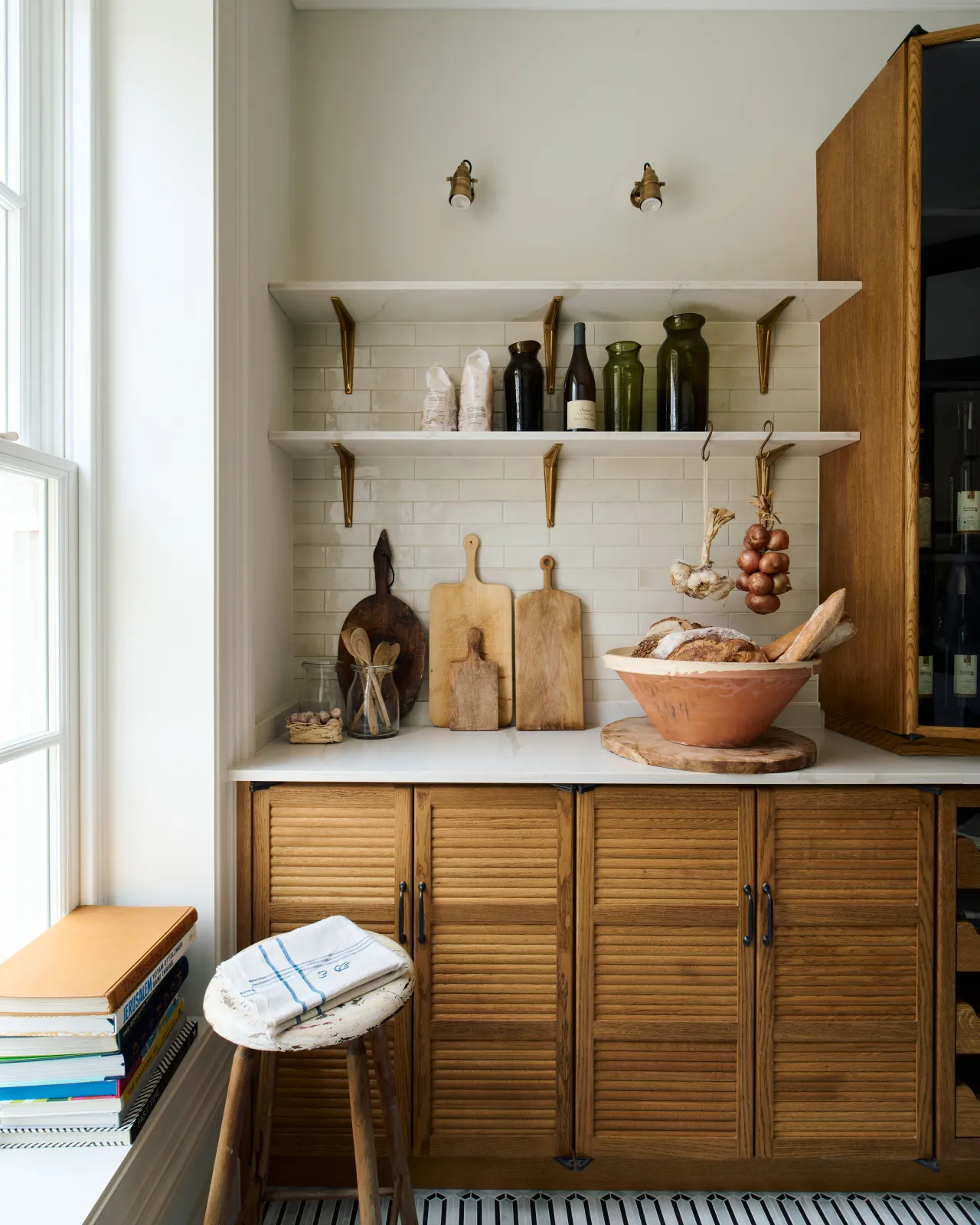 A straight-on view of a mid-century-style kitchen utility with oak cabinetry, white walls and white shelves with classic brass utilitarian shelf brackets.