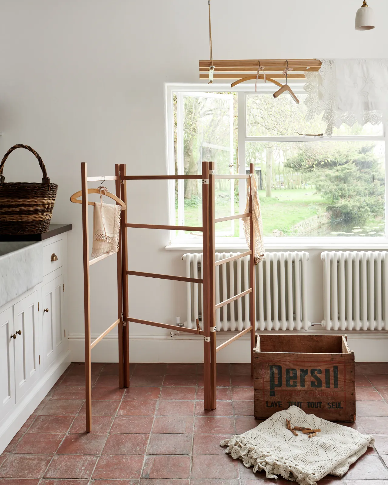 A wooden clothes horse in a Mediterranean-inspired room with white walls, terracotta flooring and rustic styling.