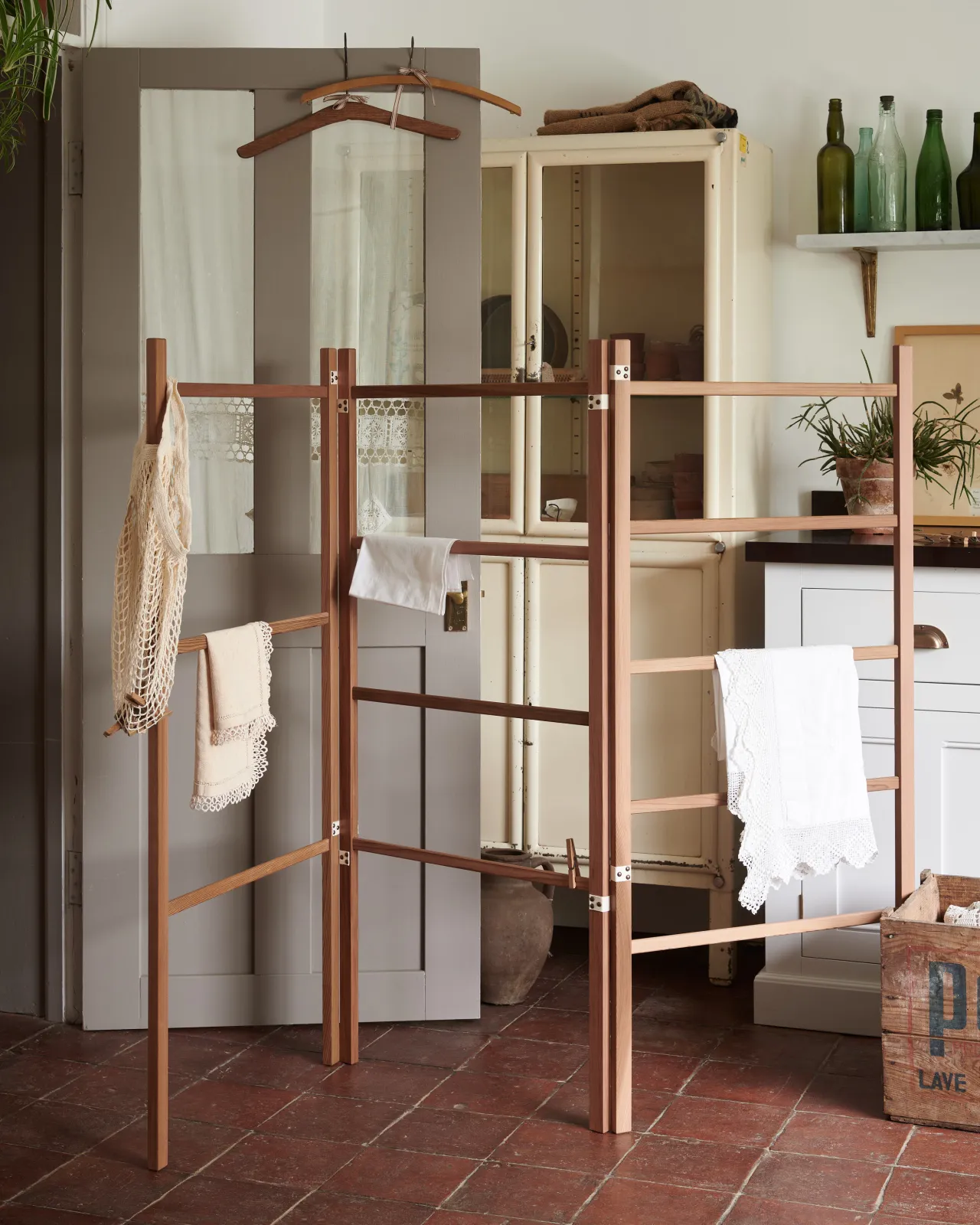 A wooden clothes horse in a Mediterranean-inspired room with white walls, terracotta flooring and rustic styling.