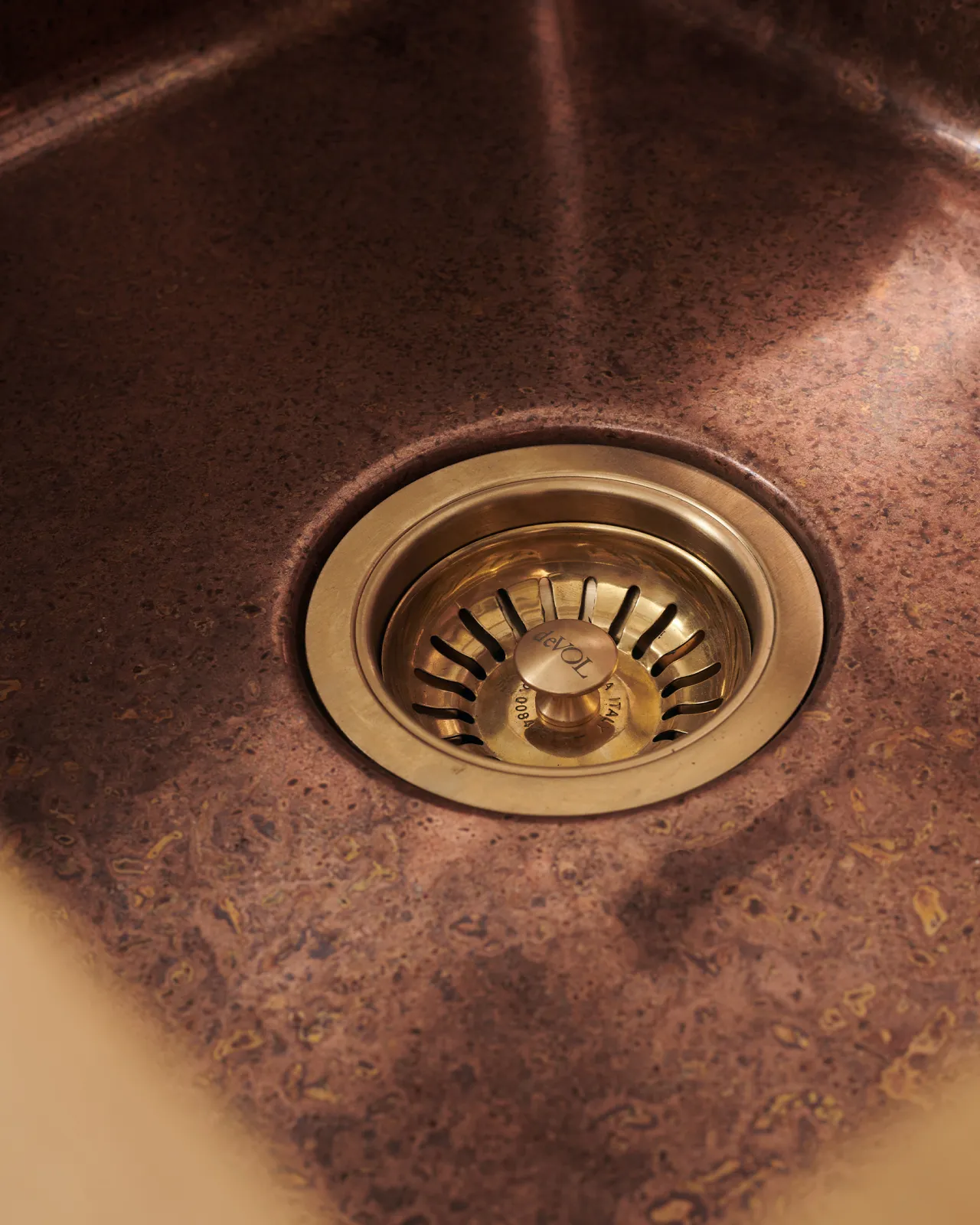 A close-up view of a brass basket waste strainer in a small undermount aged copper sink.