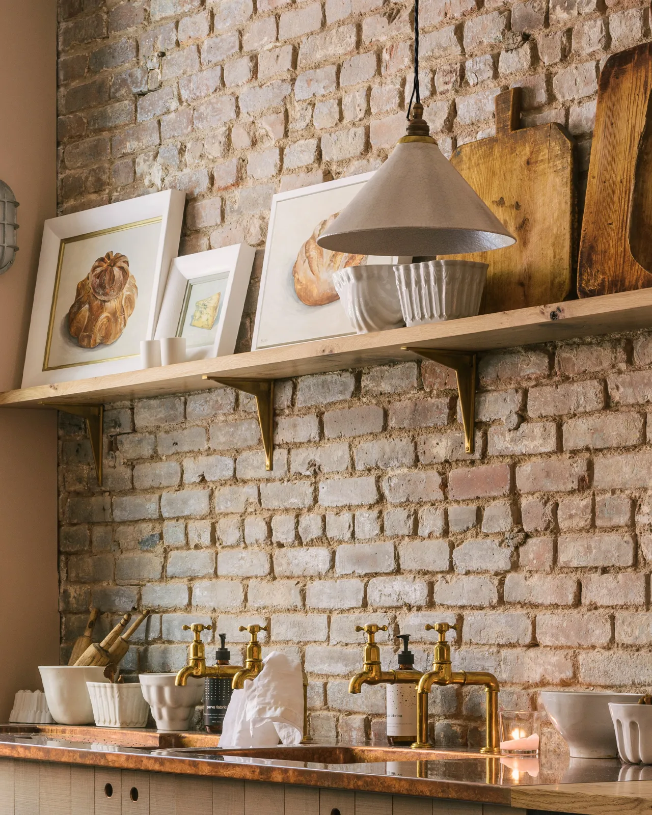 An oblique view of a white glazed ceramic pendant light with delicate crazing hanging in front of a worn brick wall with an oak shelf.
