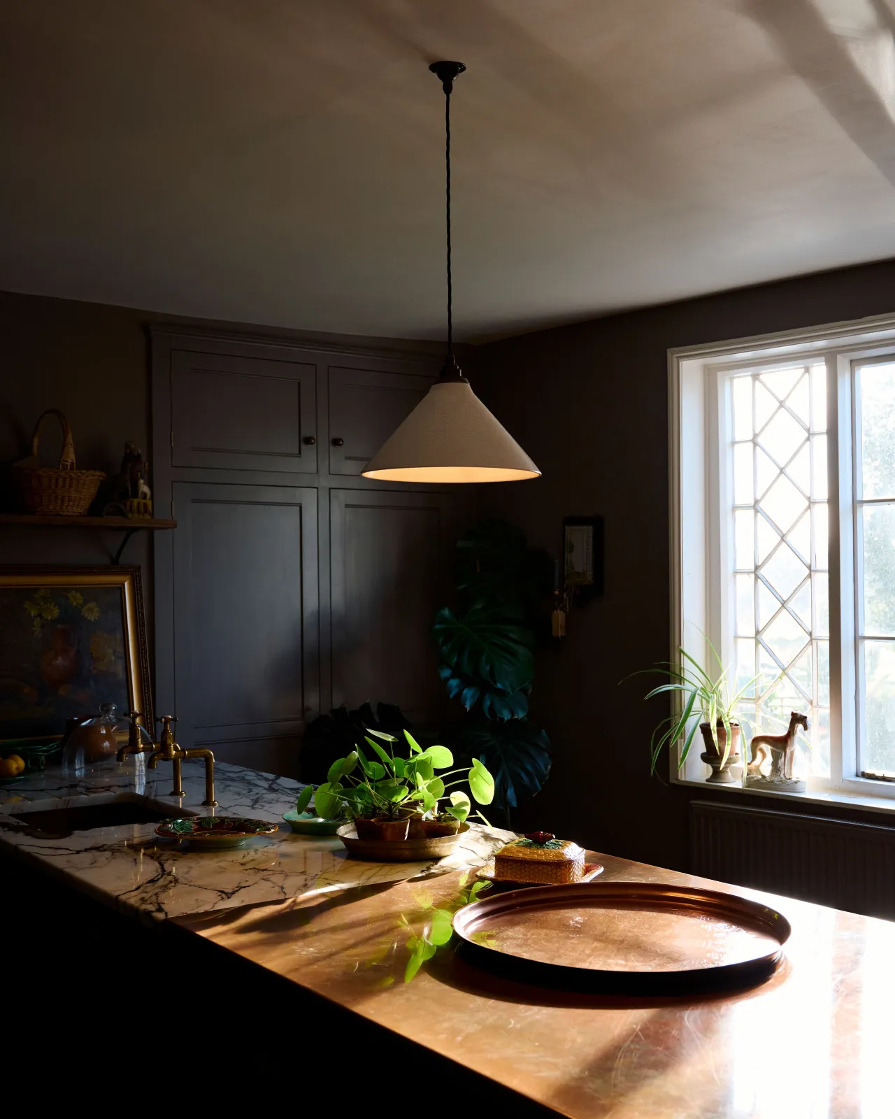 A white glazed ceramic pendant light with delicate crazing hanging in a dark room above an aged copper worktop.