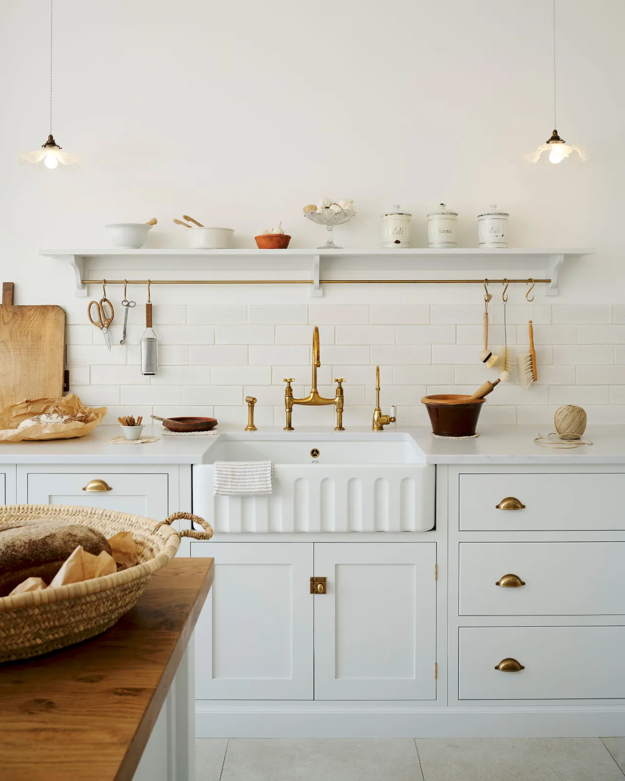 A straight-on view of a white Shaker-style kitchen with a splashback of white metro wall tiles with delicate crazing.