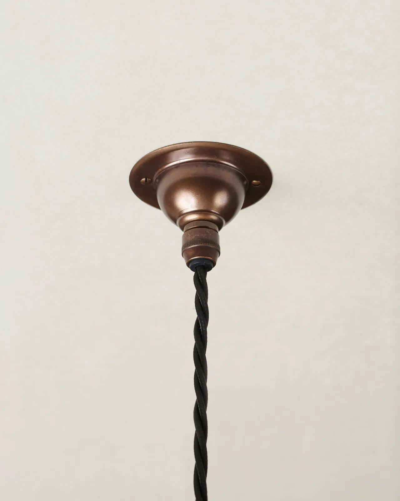 A small antiqued brass ceiling rose with a black twisted fabric flex cord.