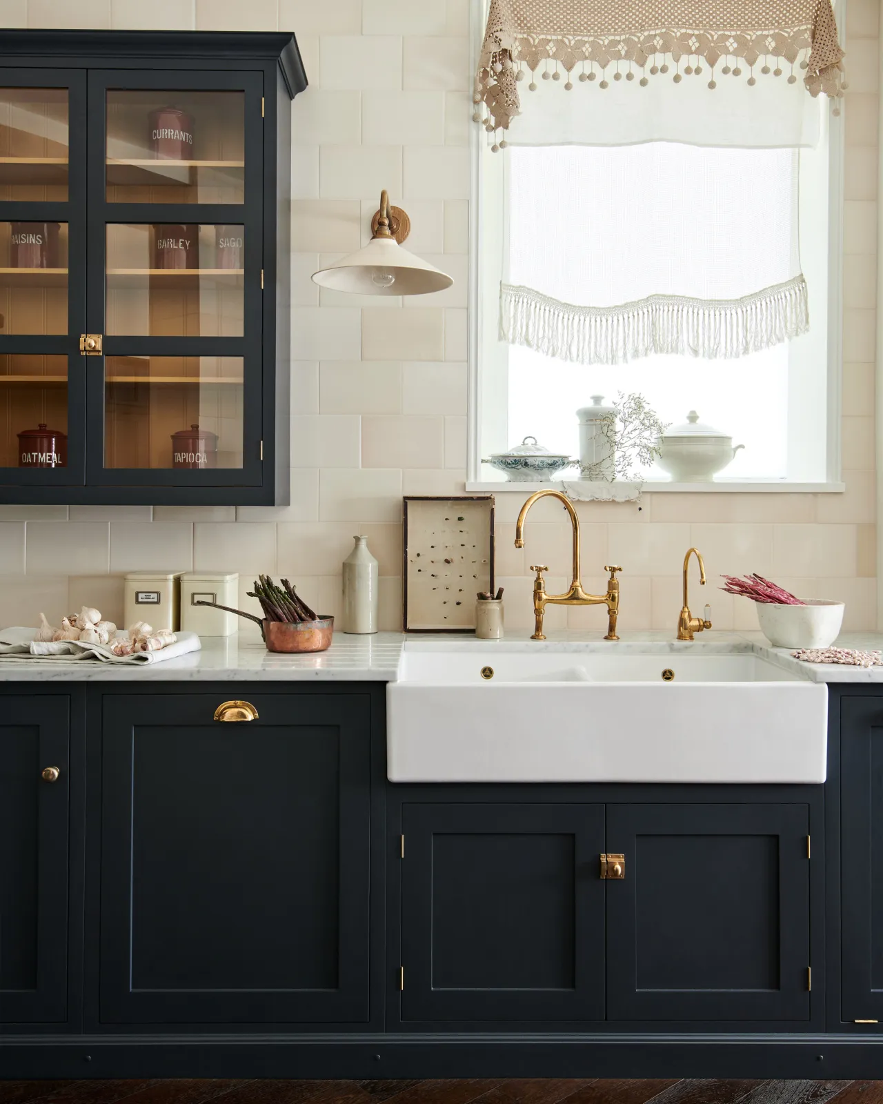 A deep blue Shaker-style kitchen with a wide ceramic Belfast sink and a wall of subtly varied cream subway tiles above.