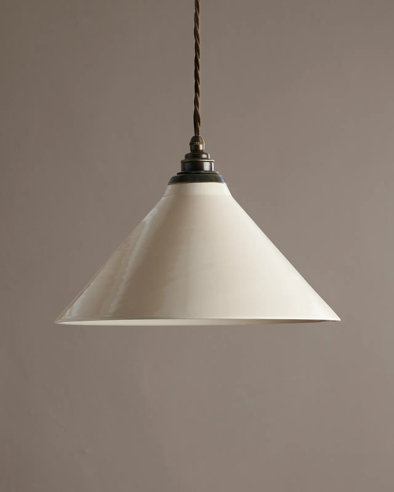 A large cream glazed ceramic pendant light with an aged brass E27 lampholder and cuff and brown twisted fabric flex cord.