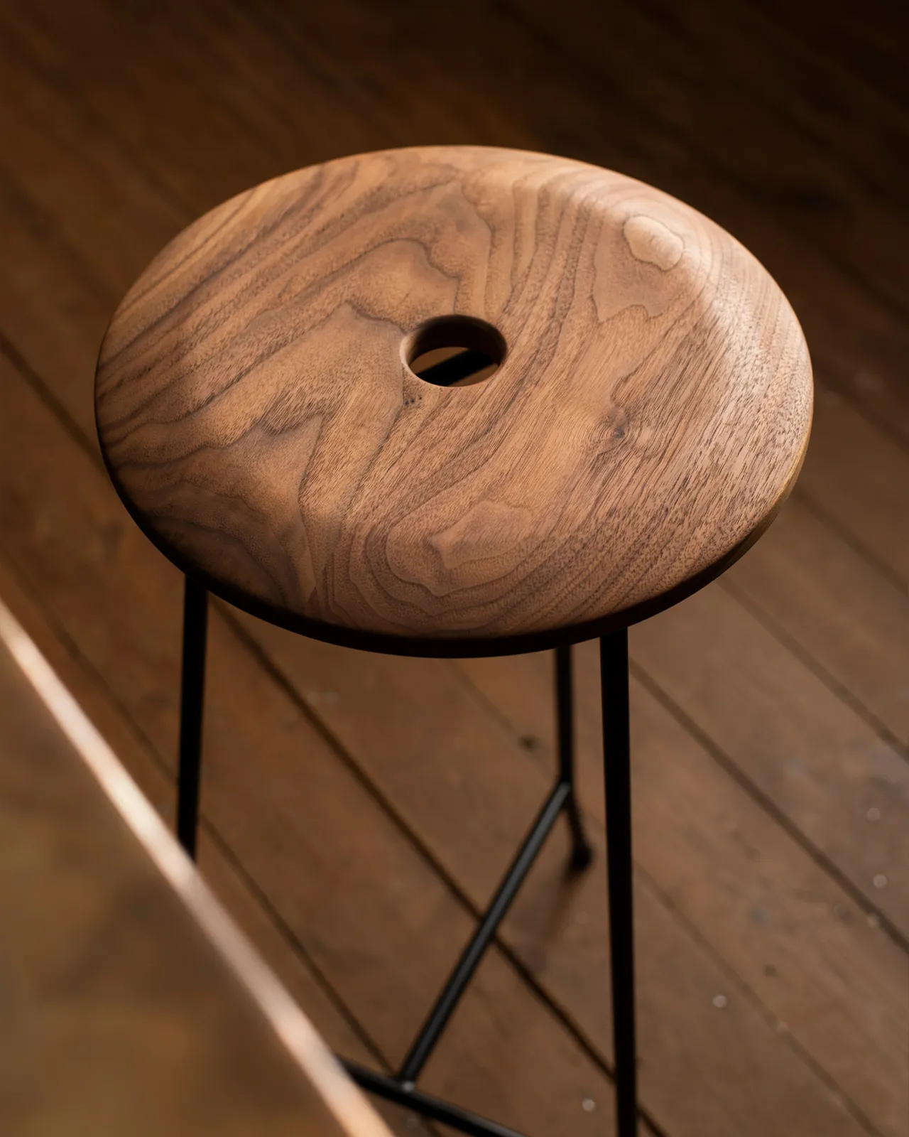 A close-up view of a round walnut seat top with a central hole and a natural oiled finish.