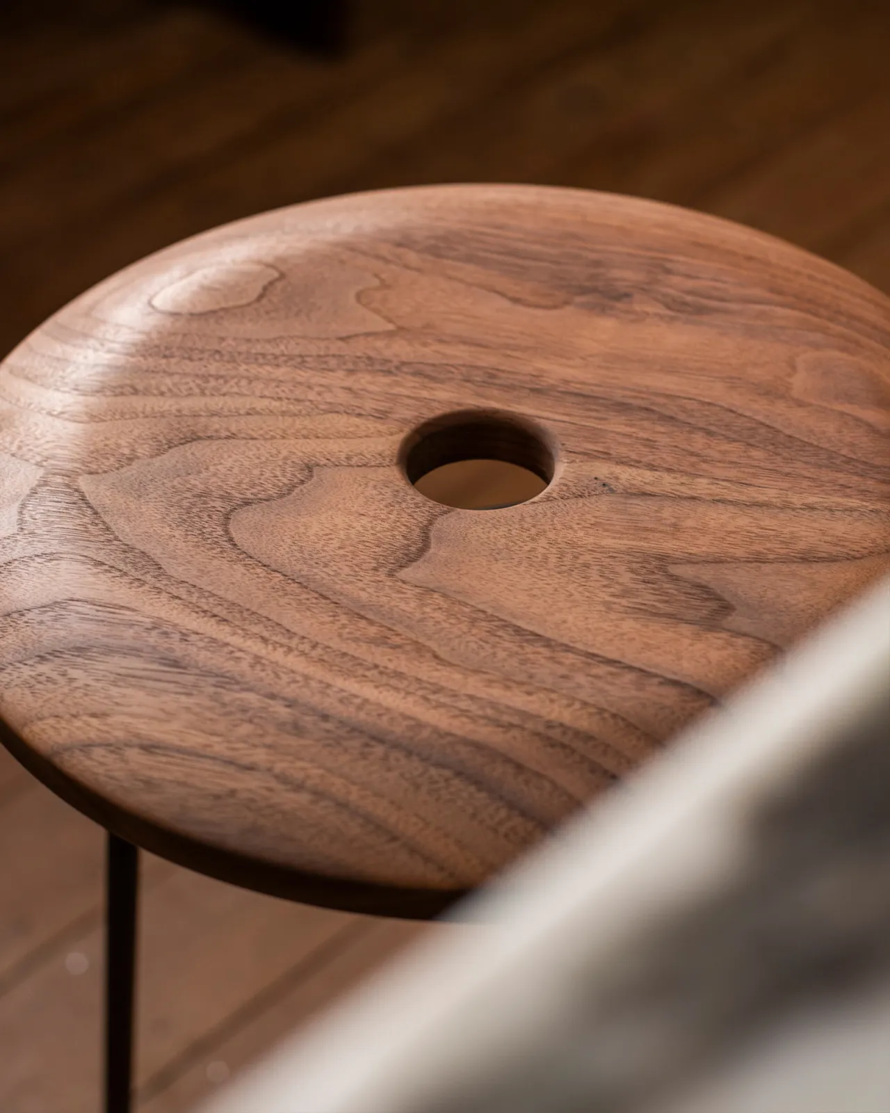 A close-up view of a round walnut seat top with a central hole and a natural oiled finish.