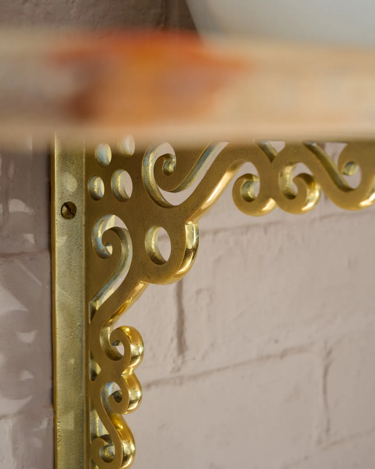 A close-up oblique view of the decorative cutout patterns on a large Victorian-inspired ornate aged brass shelf bracket.