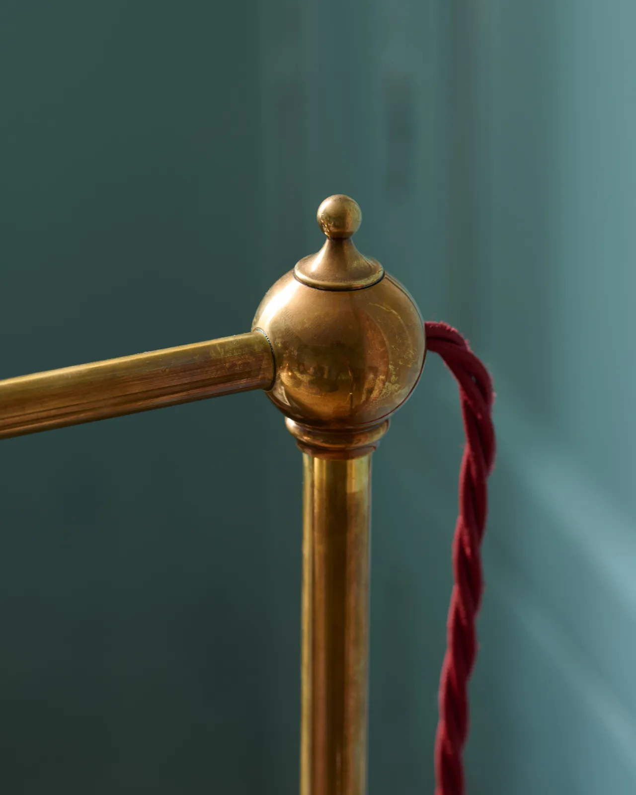 A close-up view of a pointed brass finial with red twisted fabric flex cord leading into the back.