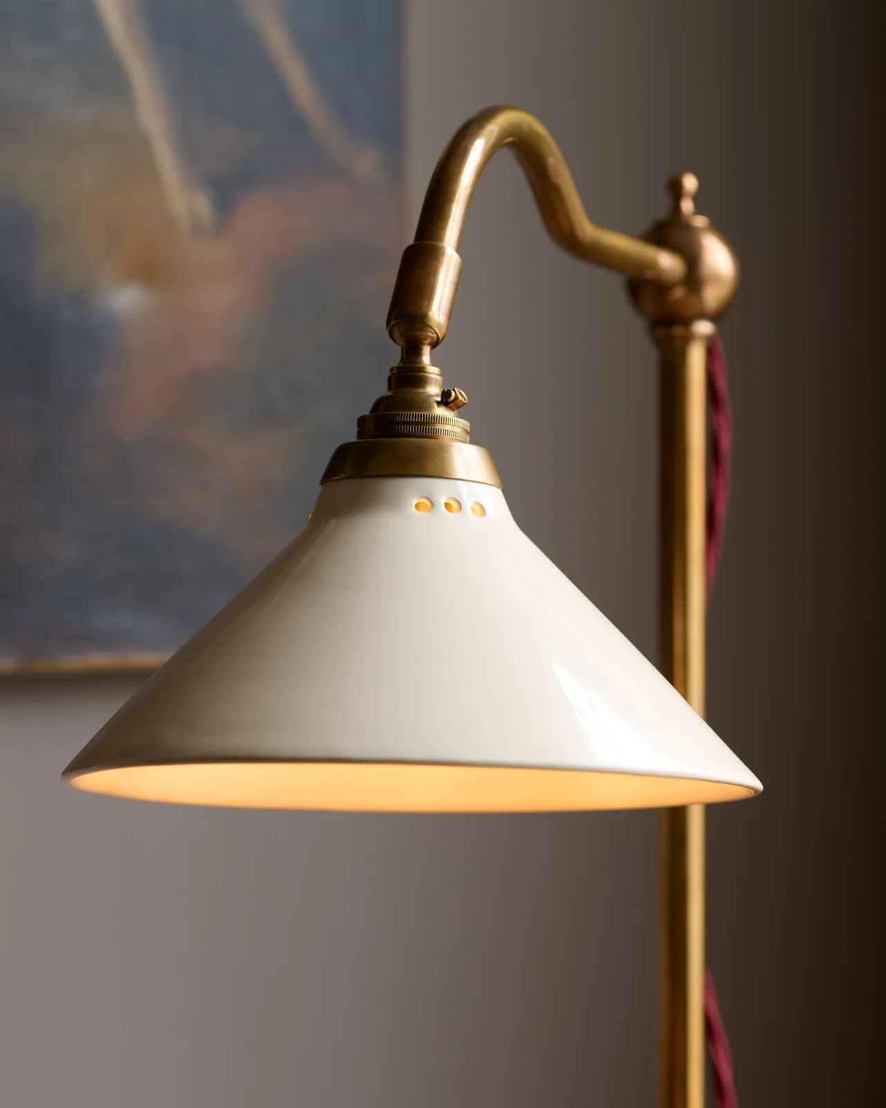 A close-up view of a small cream glazed ceramic light shade fitted to a curved brass arm with a pointed finial.