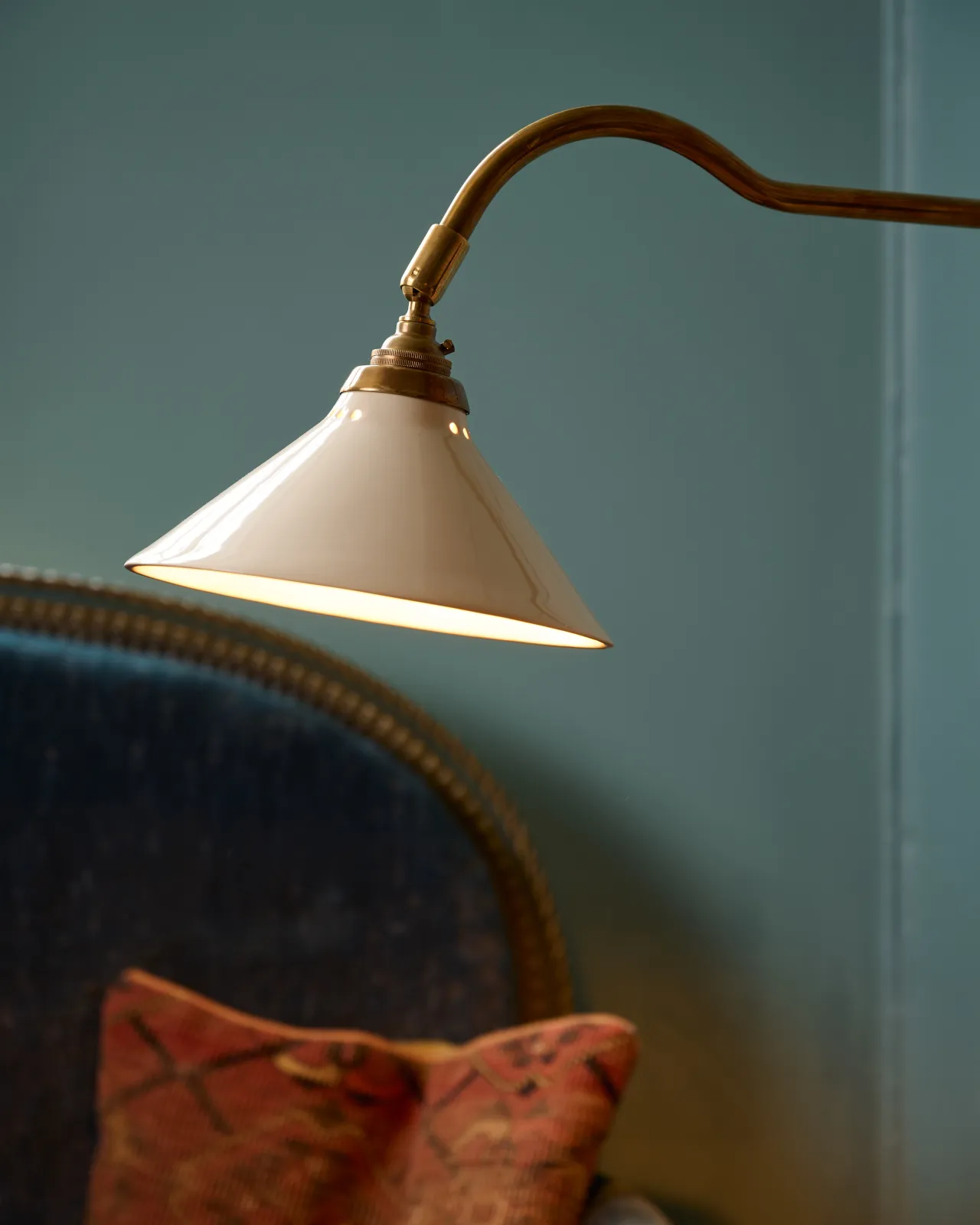 A close-up view of a small cream glazed ceramic light shade fitted to a curved brass arm.