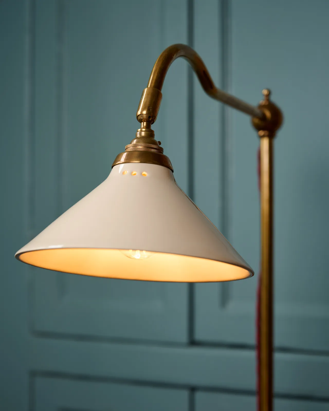 A close-up view of a small cream glazed ceramic light shade fitted to a curved brass arm with a pointed finial.
