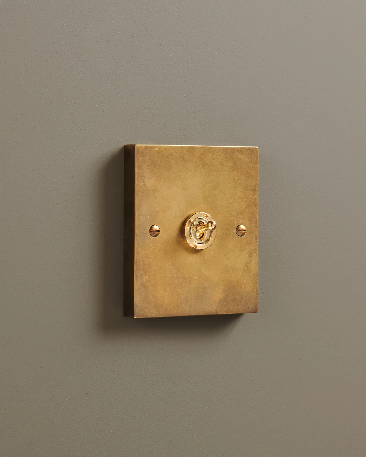 An oblique view of a 1 gang box toggle switch in a warm burnished brass finish.