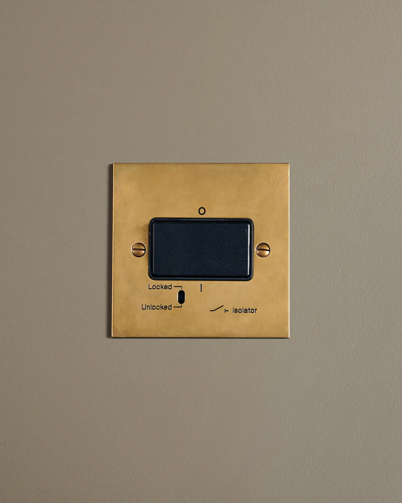 A straight-on view of a classic extractor fan isolator switch a warm burnished brass finish.