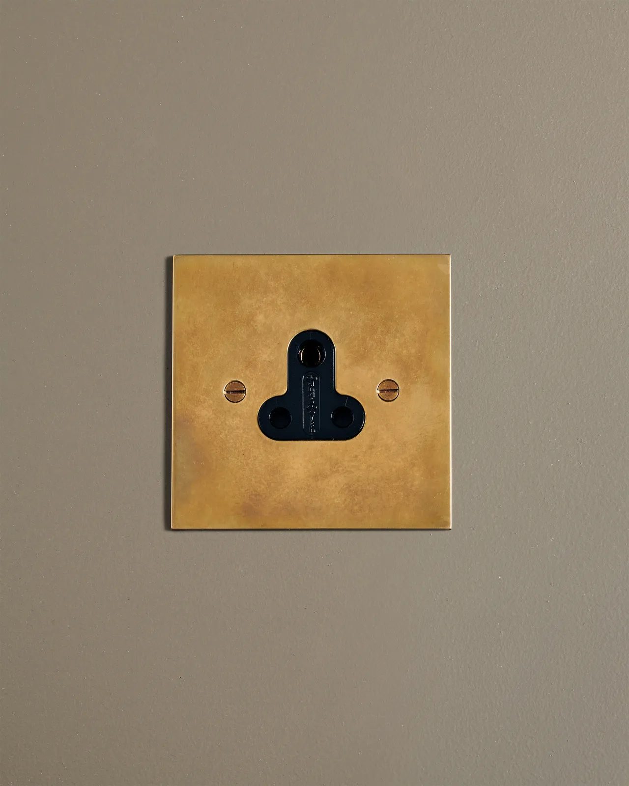 A straight-on view of a classic 5 amp single plug socket in a warm burnished brass finish.