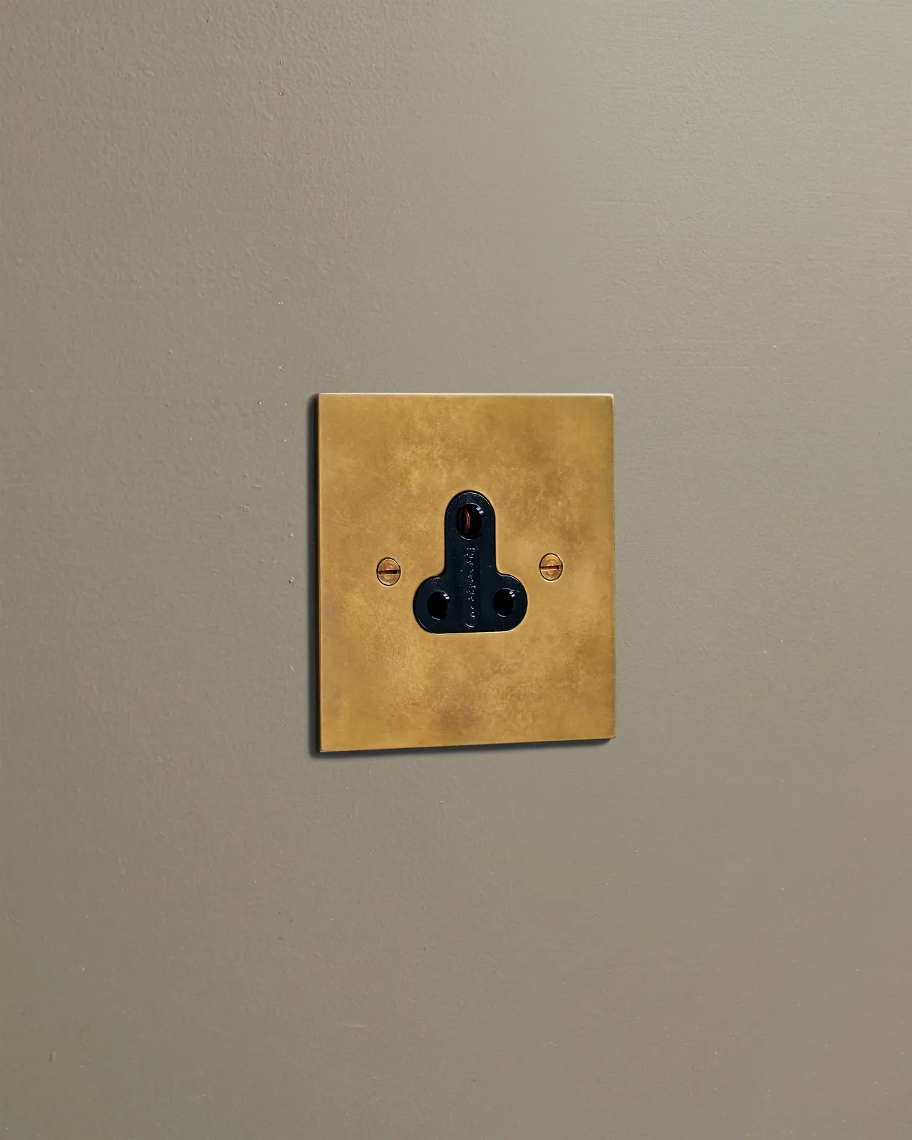 An oblique view of a classic 5 amp single plug socket in a warm burnished brass finish.