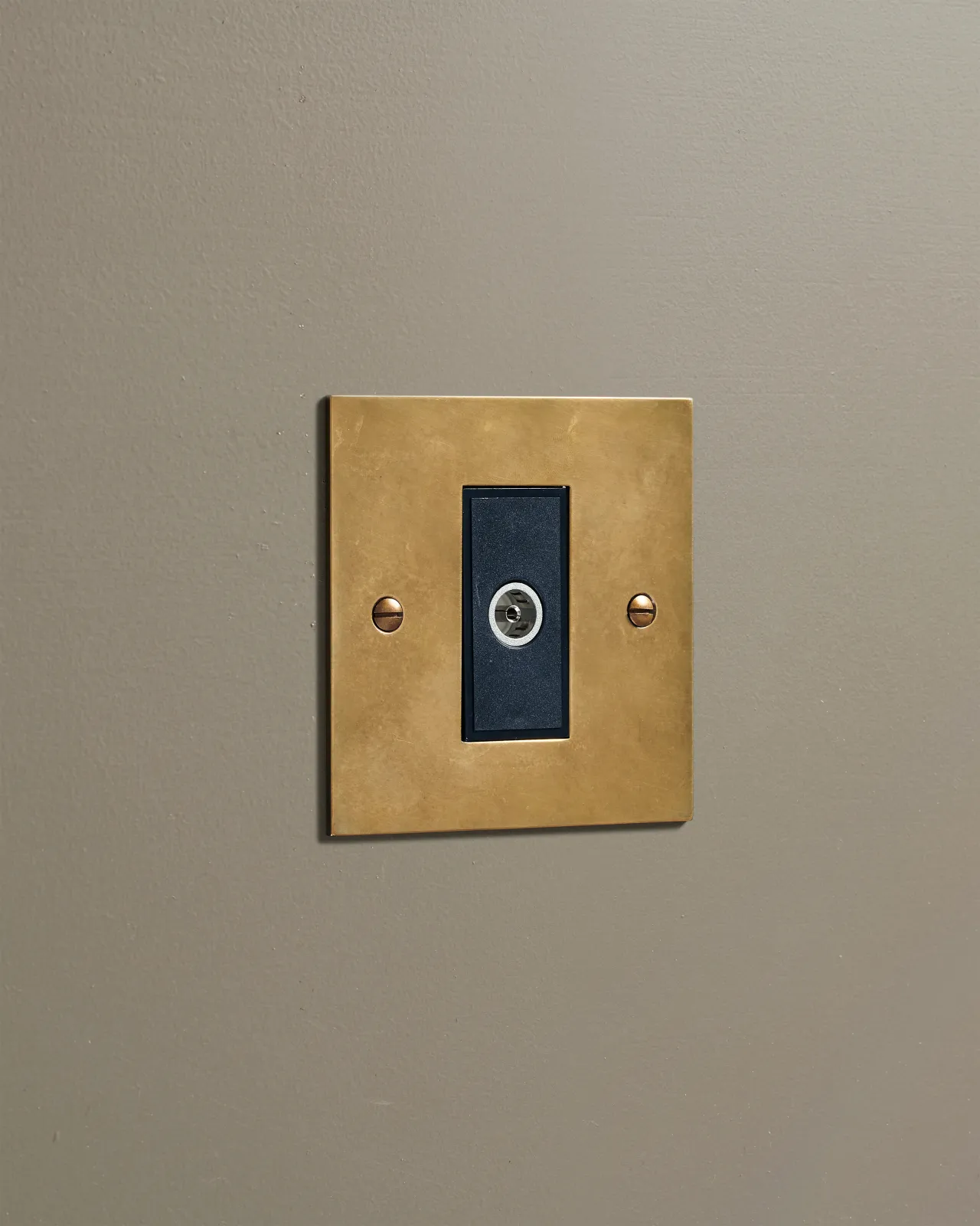 An oblique view of a classic single coaxial TV socket in a warm burnished brass finish.