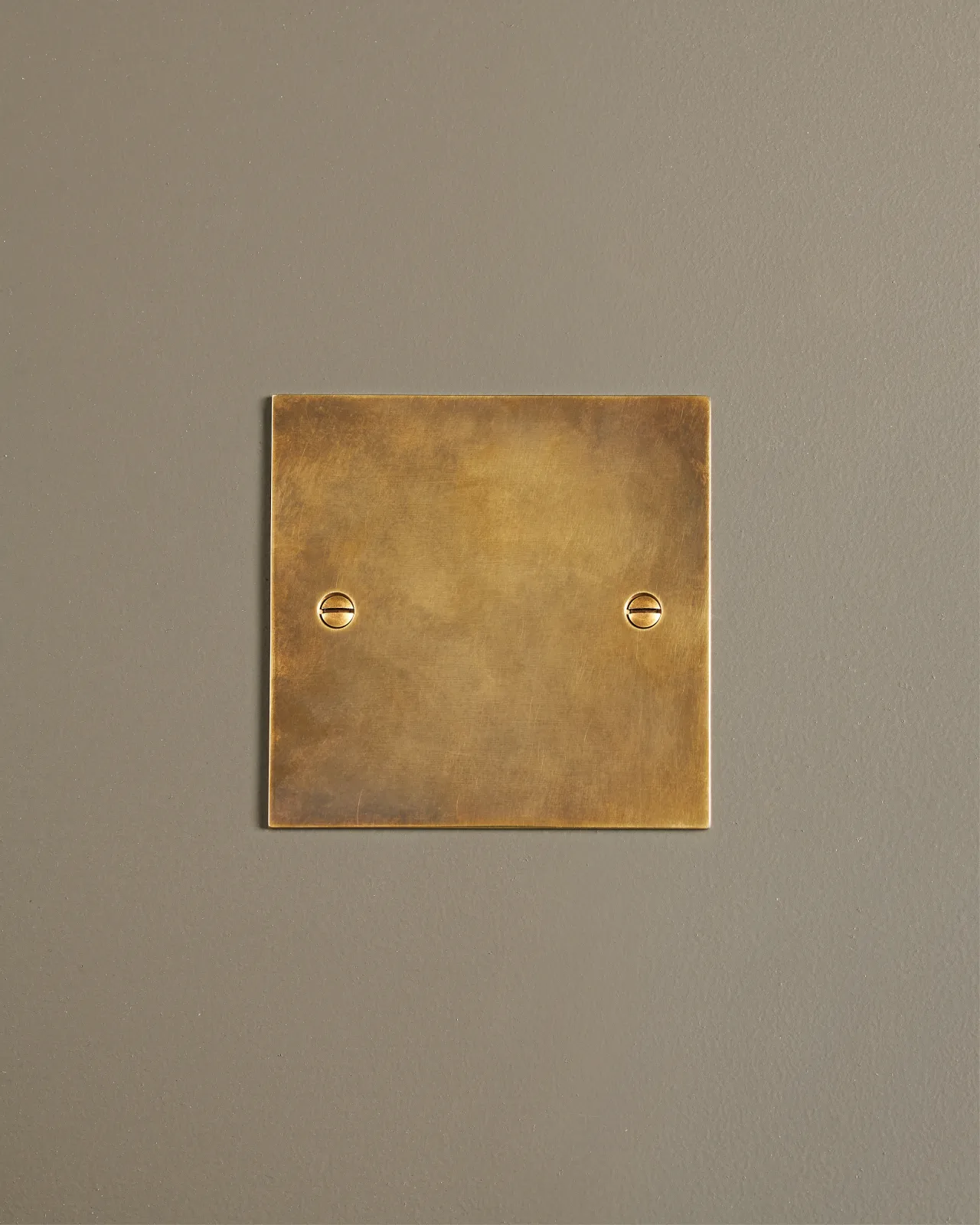 A straight-on view of a classic blank socket plate in a warm burnished brass finish.