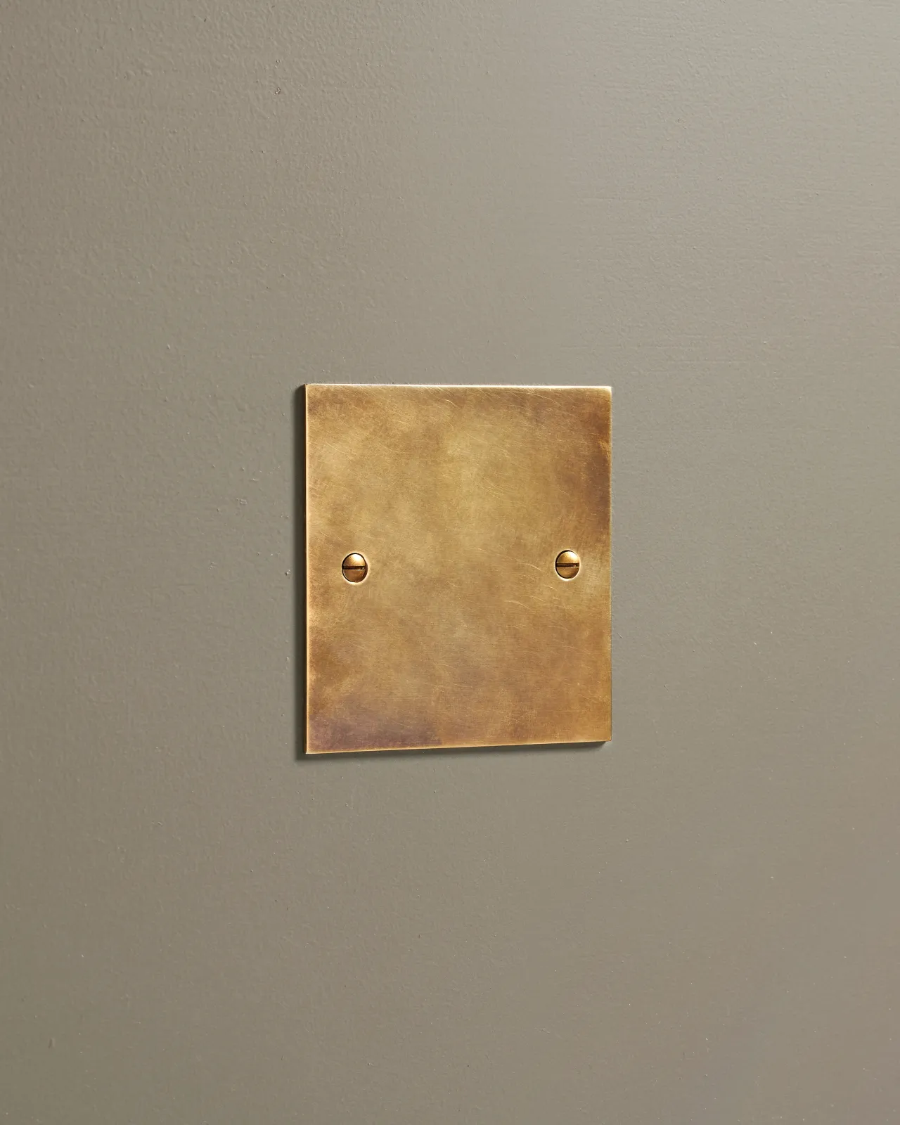 An oblique view of a classic blank socket plate in a warm burnished brass finish.