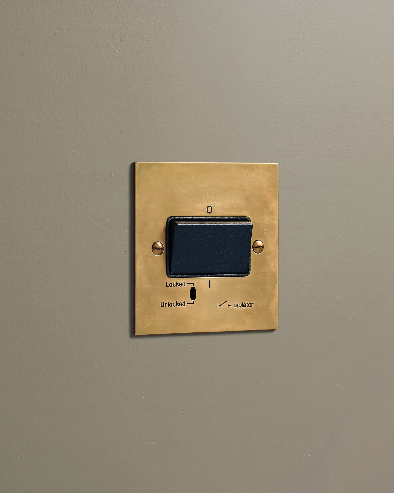 An oblique view of a classic extractor fan isolator switch in a warm burnished brass finish.