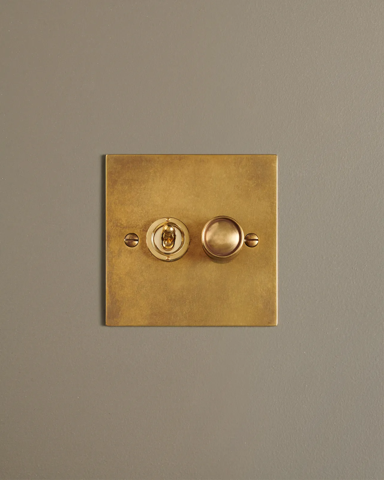 A straight-on view of a 2 gang classic toggle and dimmer mixed switch in a warm burnished brass finish.