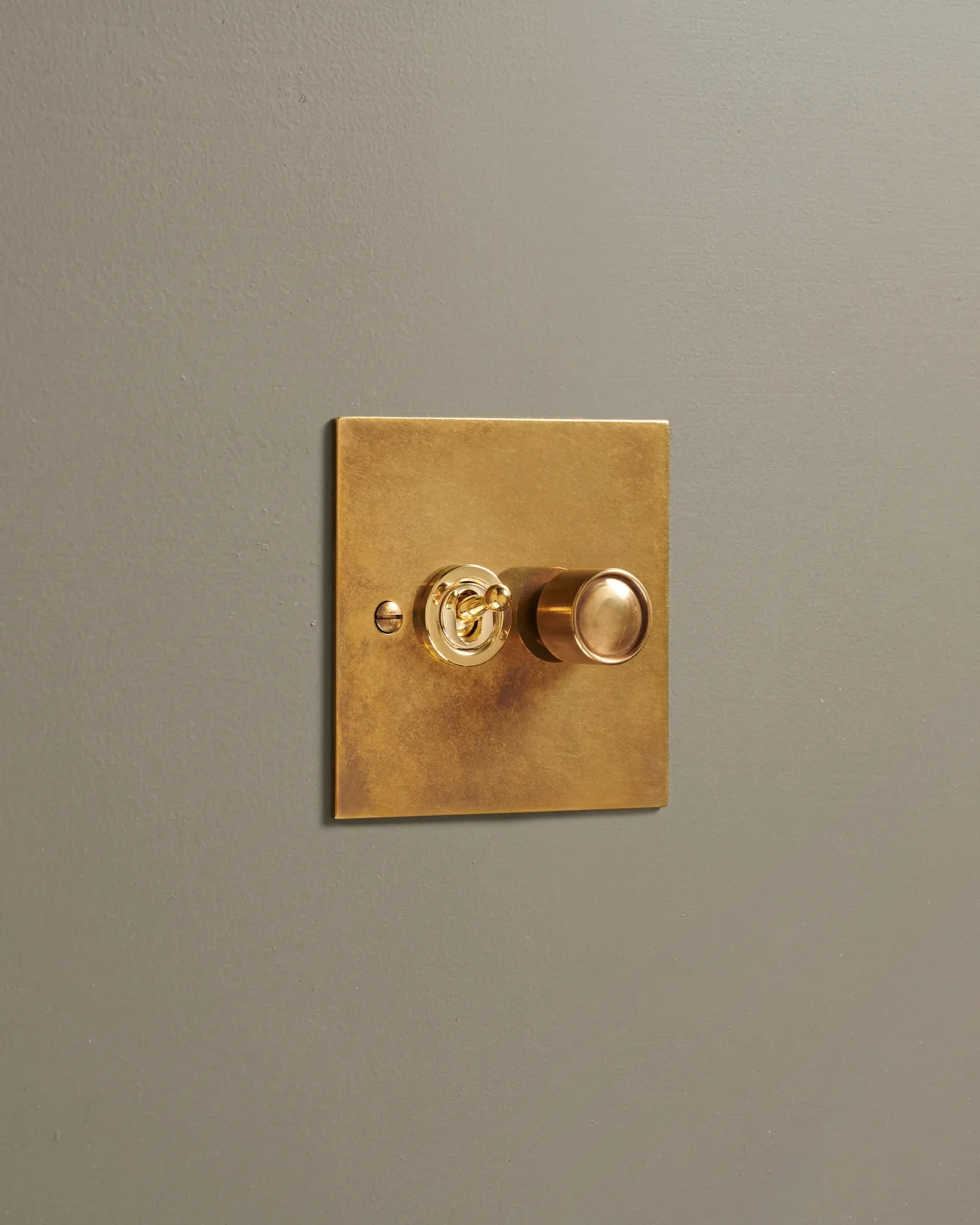An oblique view of a 2 gang classic toggle and dimmer mixed switch in a warm burnished brass finish.