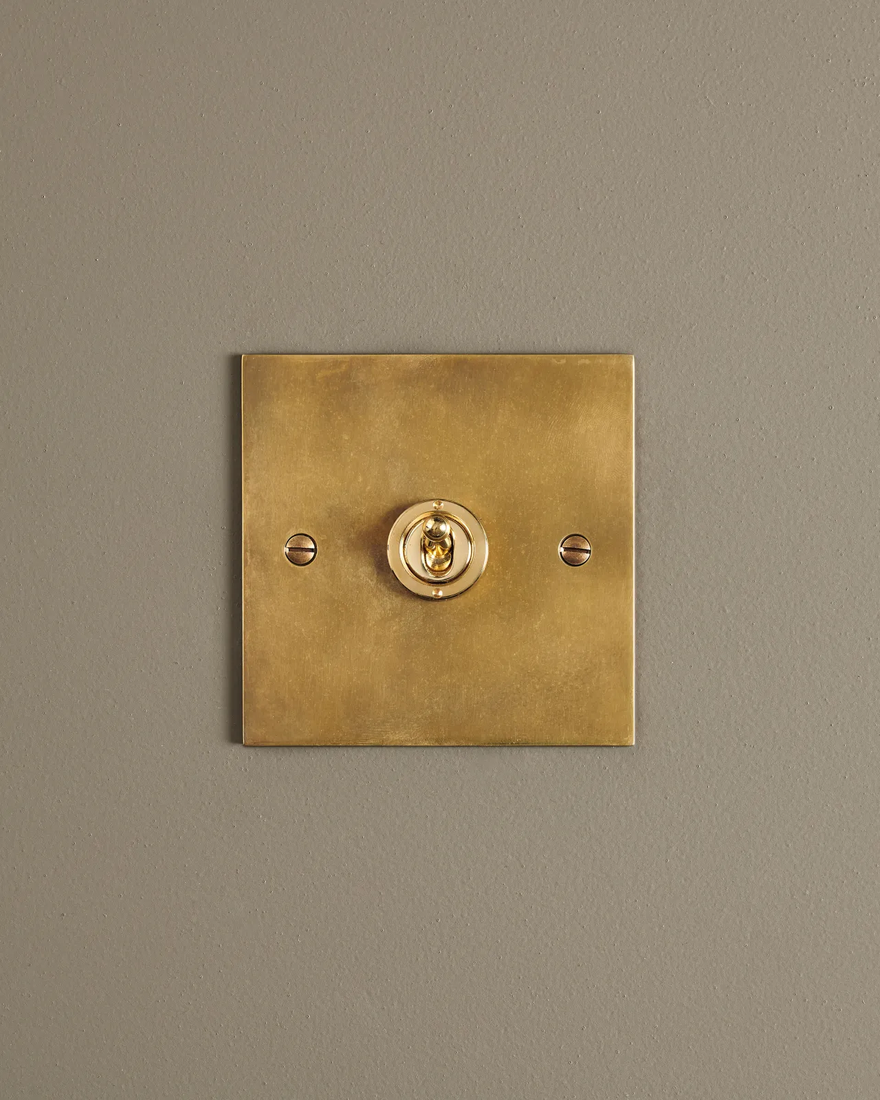 A straight-on view of a 1 gang classic toggle switch in a warm burnished brass finish.
