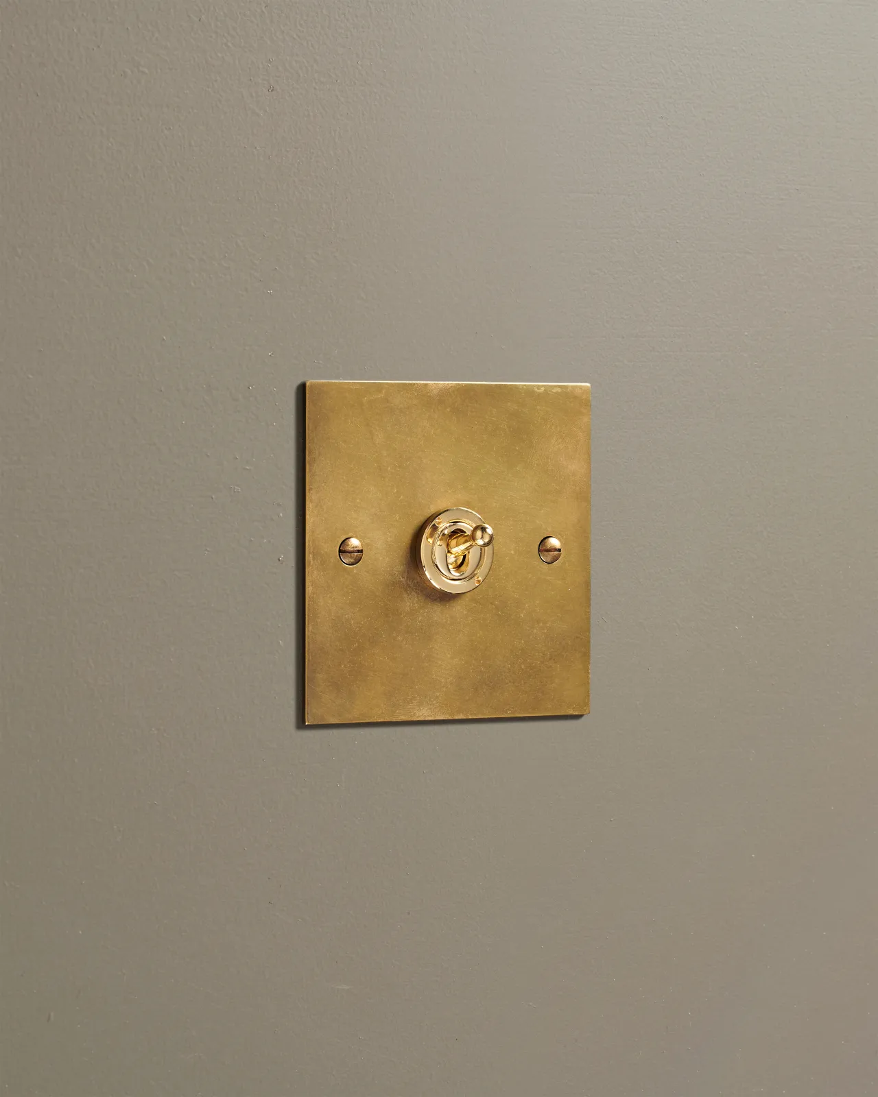 An oblique view of a 1 gang classic toggle switch in a warm burnished brass finish.