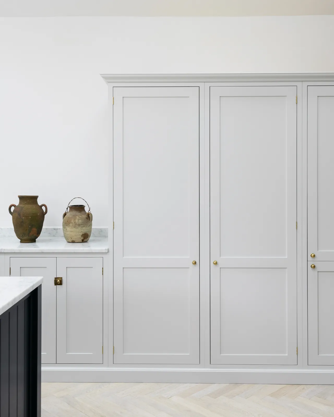 A straight-on view of a simple Shaker-style kitchen with off-white painted tall pantry cupboards and white walls.