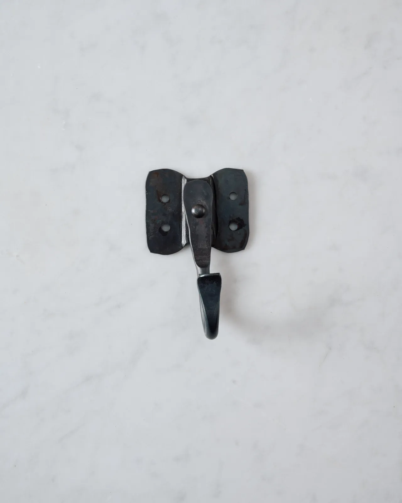 A front profile view of a large iron wall hook with a backplate shaped like elephant ears.