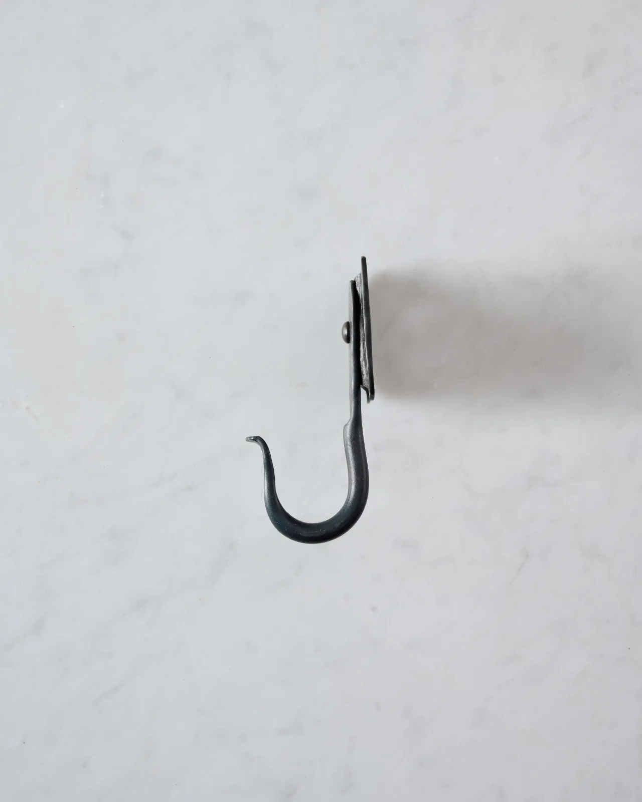 A side profile view of a large iron wall hook with a backplate shaped like elephant ears.