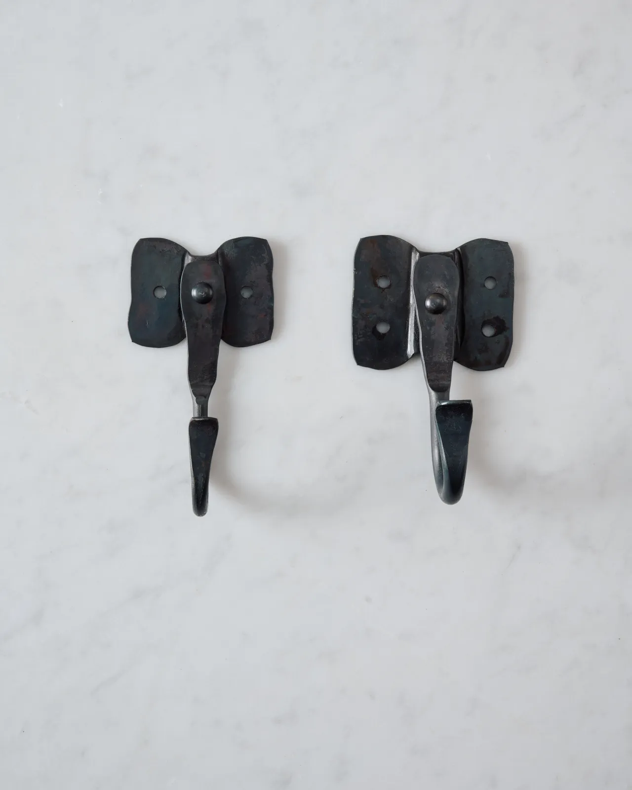 Two iron wall hooks with backplates shaped like elephant ears, one small and one large.
