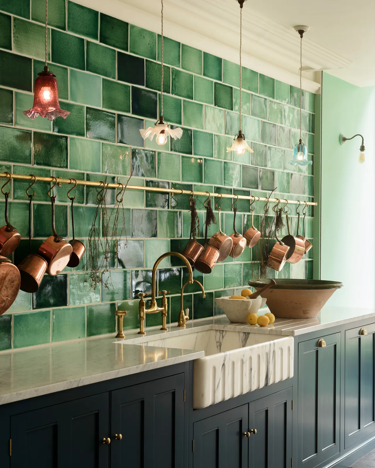 An oblique view of a large installation of handmade glossy emerald green wall tiles above a grand Arabescato marble sink and royal blue painted Georgian-style kitchen cupboards. 