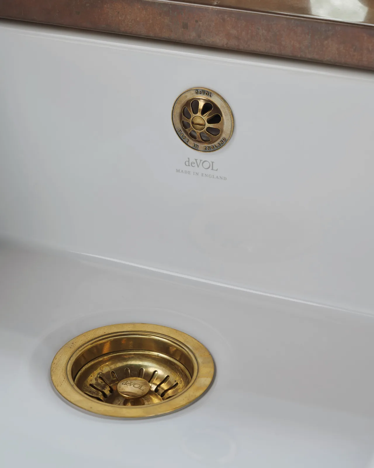 An oblique view of a basket waste strainer with a deVOL domed overflow cap in a warm burnished brass finish, there is a small 'deVOL' logo in the middle of the waste strainer finial.