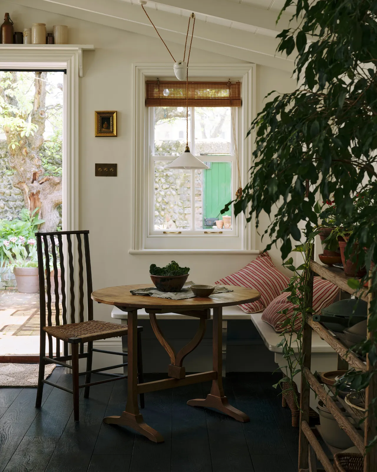 A small round pine dining table in a bench seat corner of a kitchen with white walls and dark floorboards.