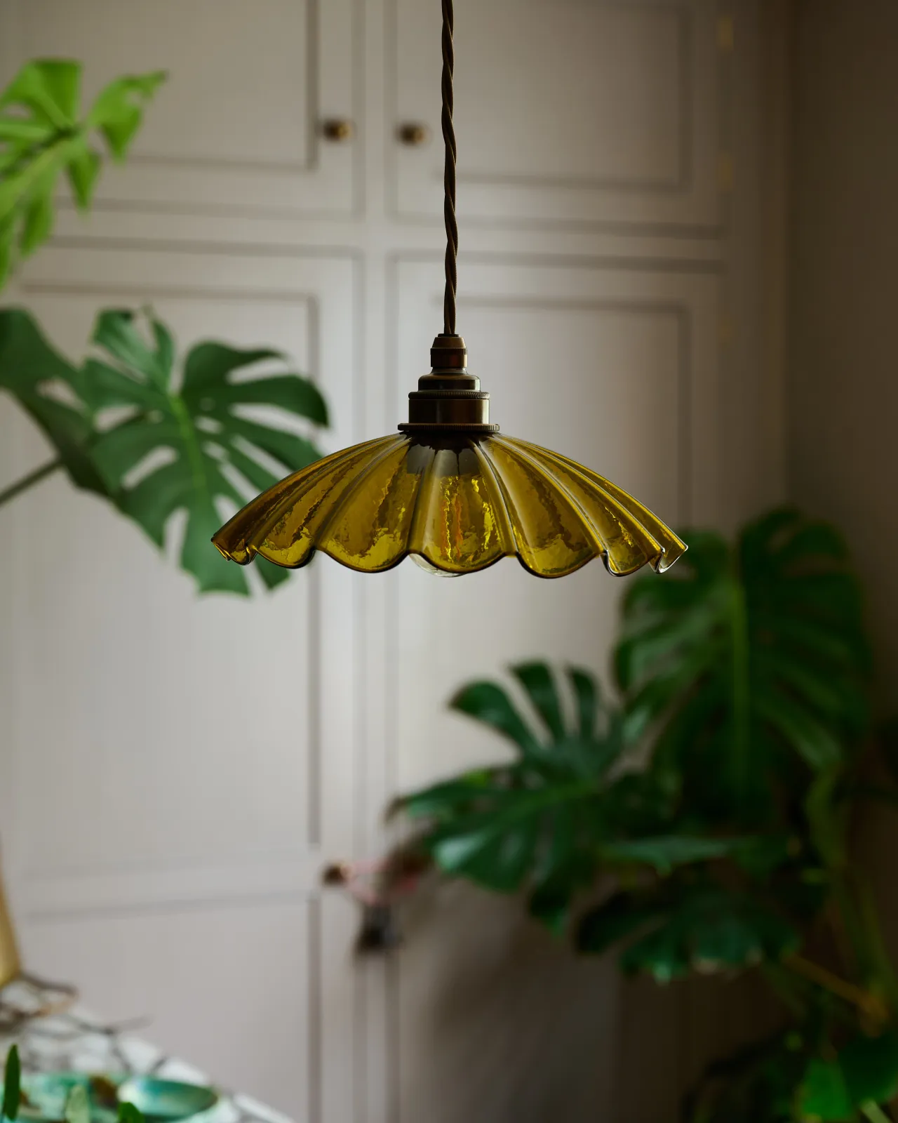 A small frilly chartreuse glass pendant light with brass fittings and brown twisted fabric flex cord. The light is off.