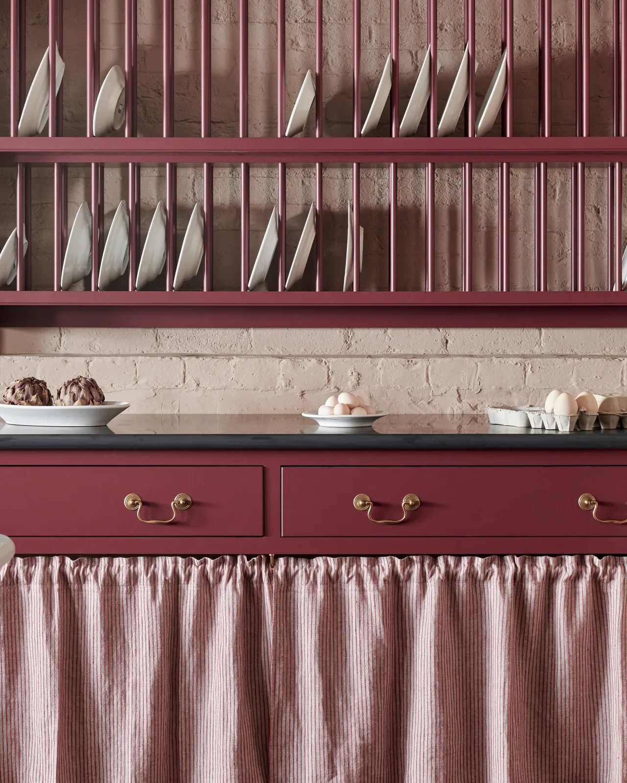 A close-up straight-on view of Georgian-style swing handles in a burnished 'Bella' brass finish, fitted to a wine red painted drawer front.