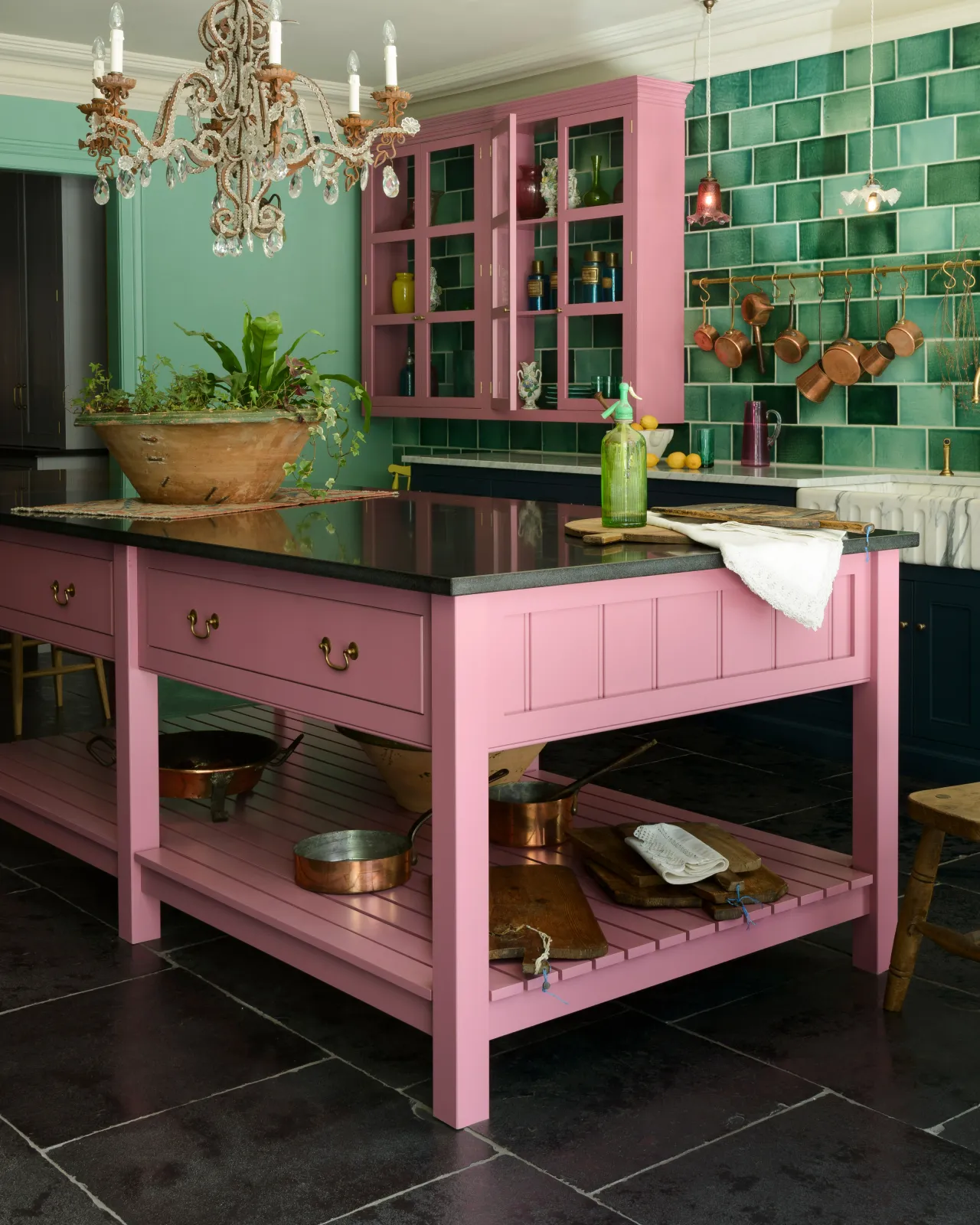 An oblique view of a eclectic Georgian-style kitchen with arsenic green walls and a pink painted prep table with a black granite worktop and Georgian-style swing handles in a burnished 'Bella' brass finish.