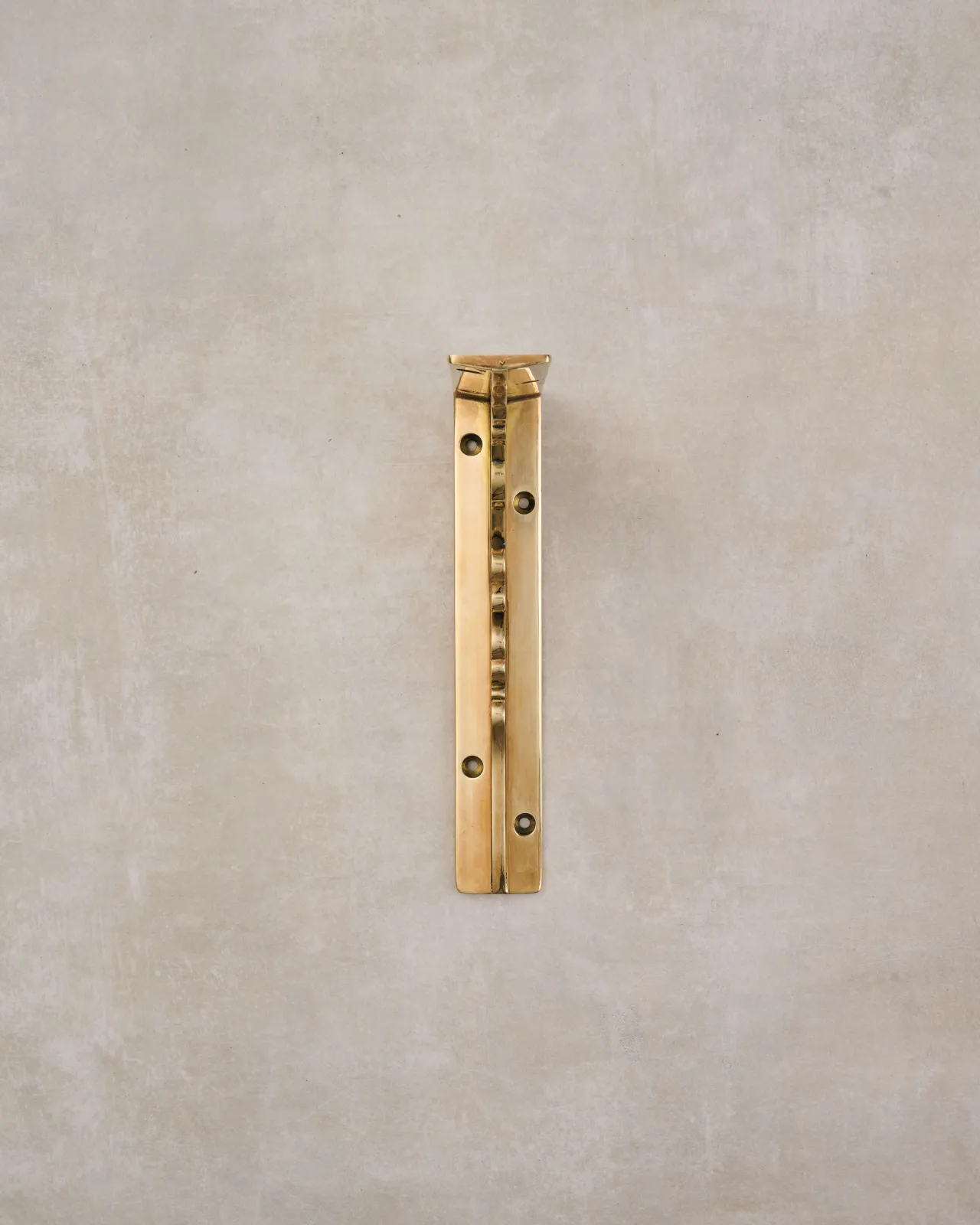 A front profile view of a small Victorian-inspired ornate shelf bracket in a warm polished brass finish.